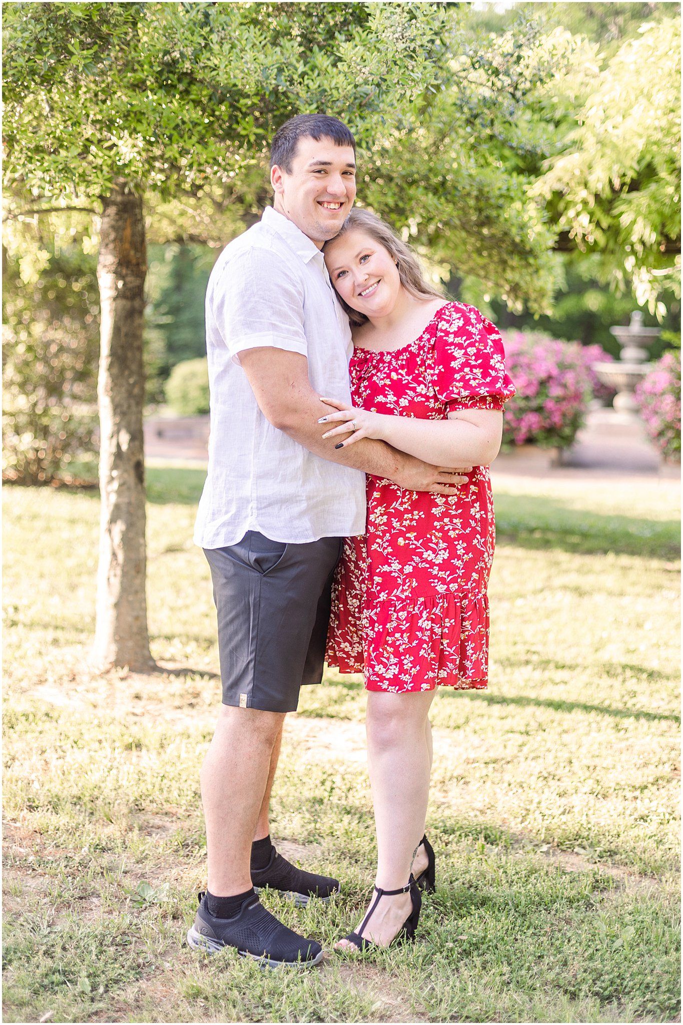 Sweet couple embracing outdoors with trees and pink flowers in background.