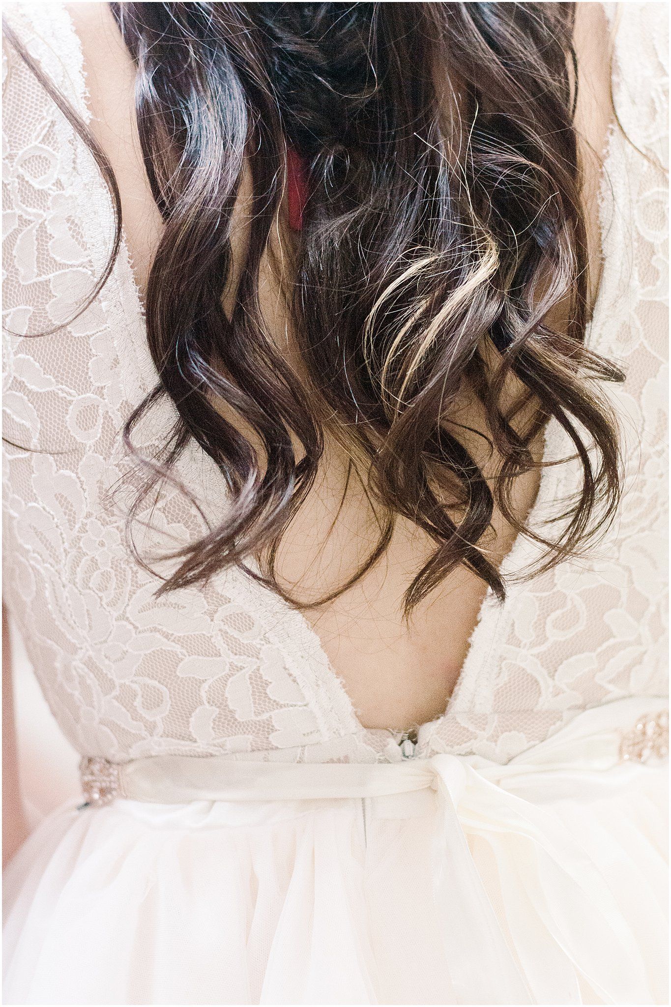 Close-up of brunette wavy hair against white lace wedding dress showing elegant back detail.
