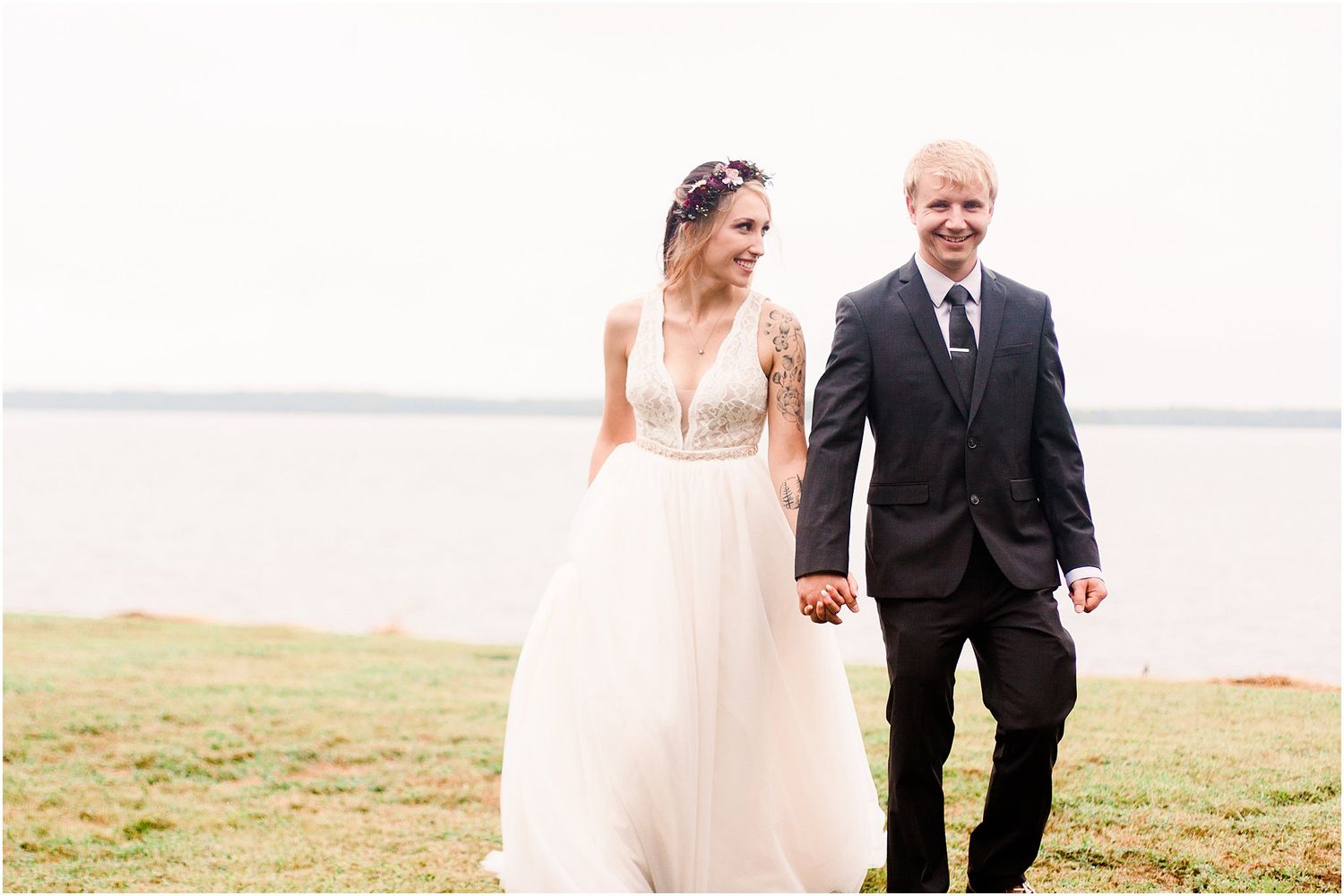 Couple walking together on grassy waterfront during their wedding day.