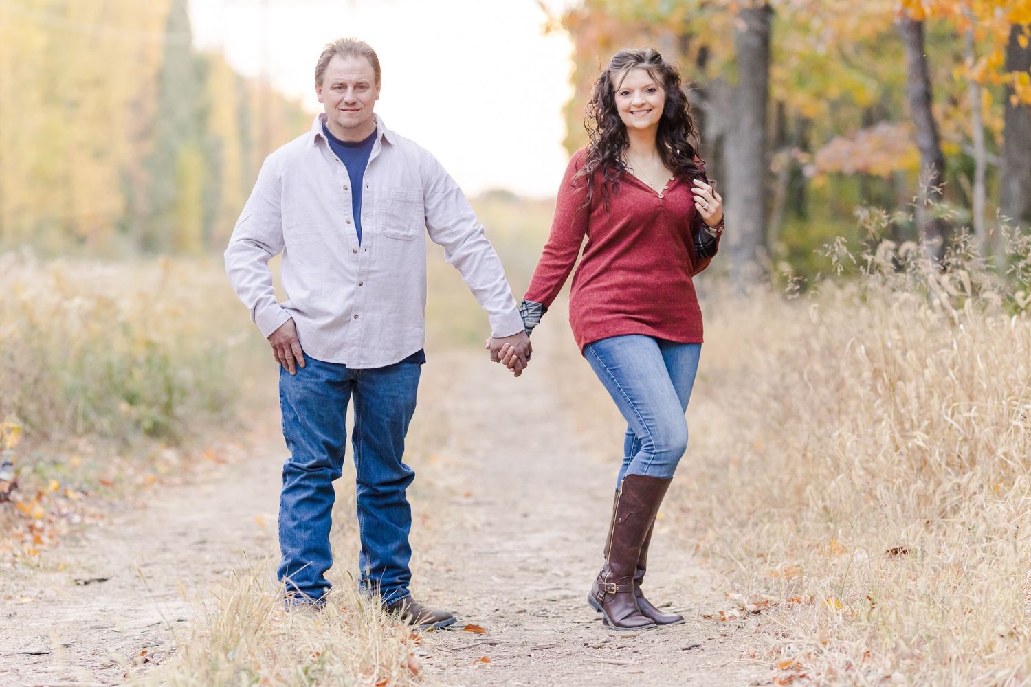 A couple walking hand in hand on a fall path wearing casual clothing and boots.