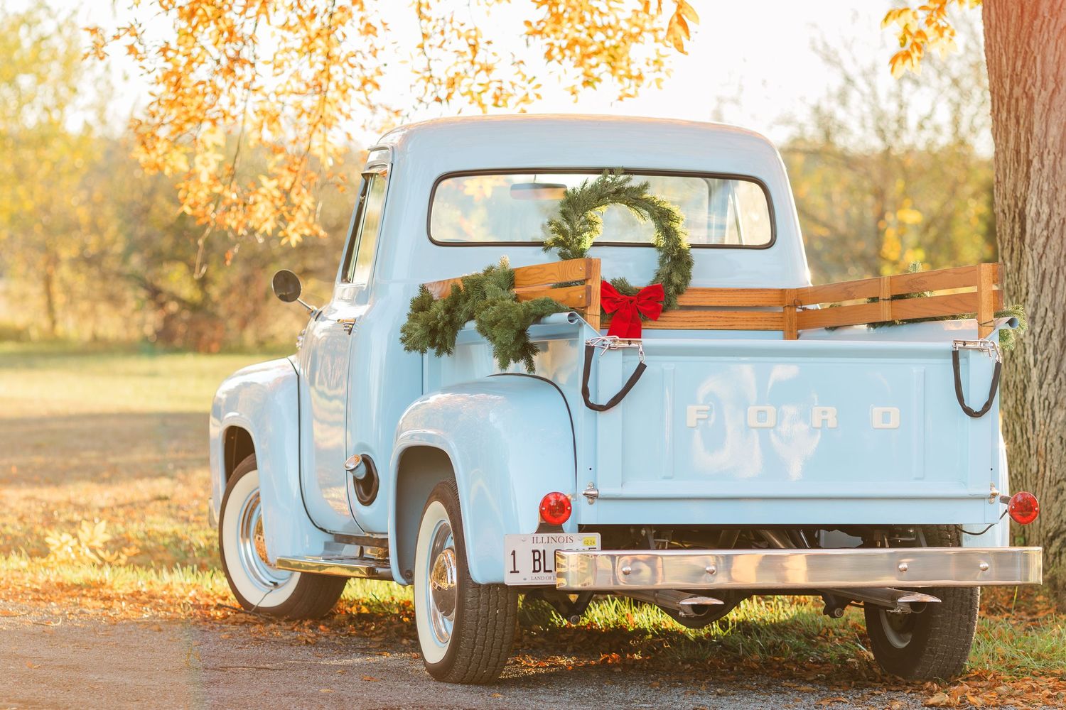 A vintage light blue pickup truck decorated with greenery sits in golden autumn light.