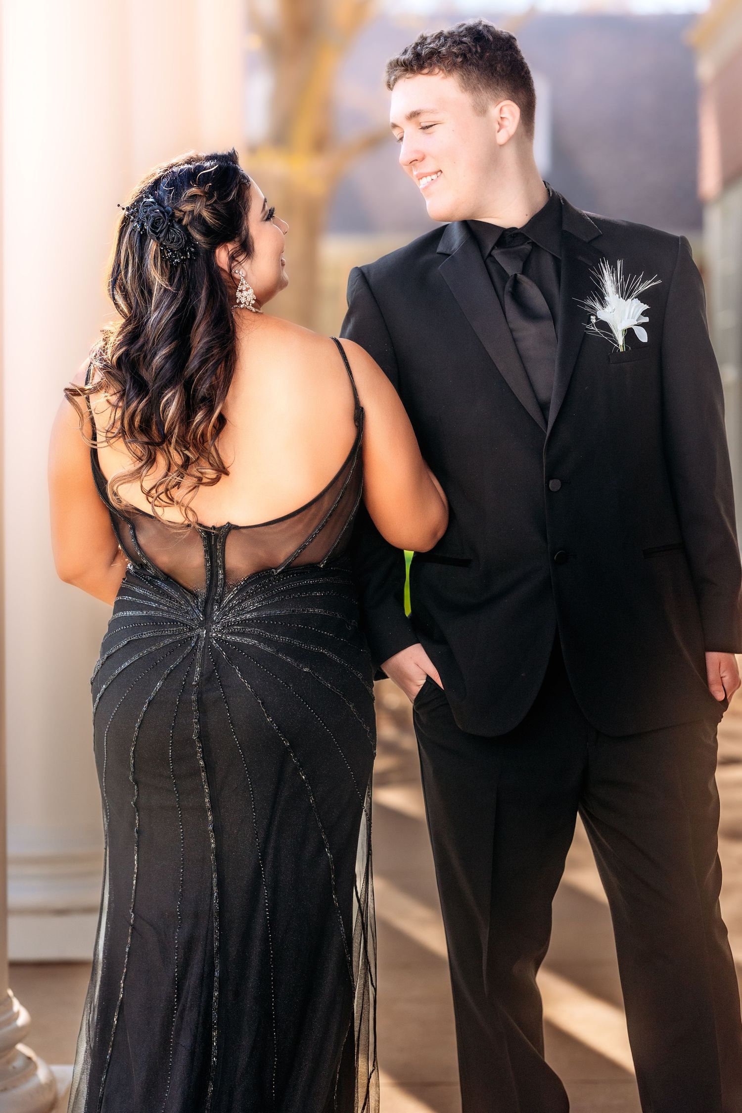 A couple in formal attire dances together, with the woman wearing a black dress and the man in a dark suit.