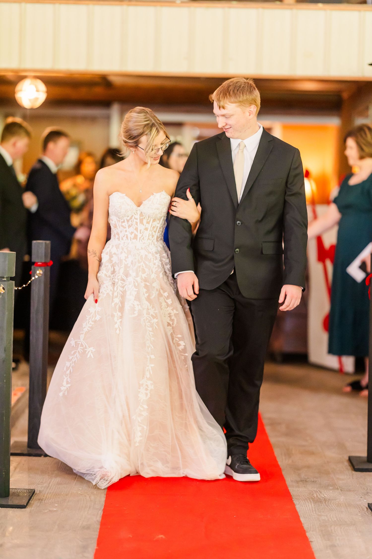 Couples walking down a red carpet in formal attire at an elegant indoor venue.