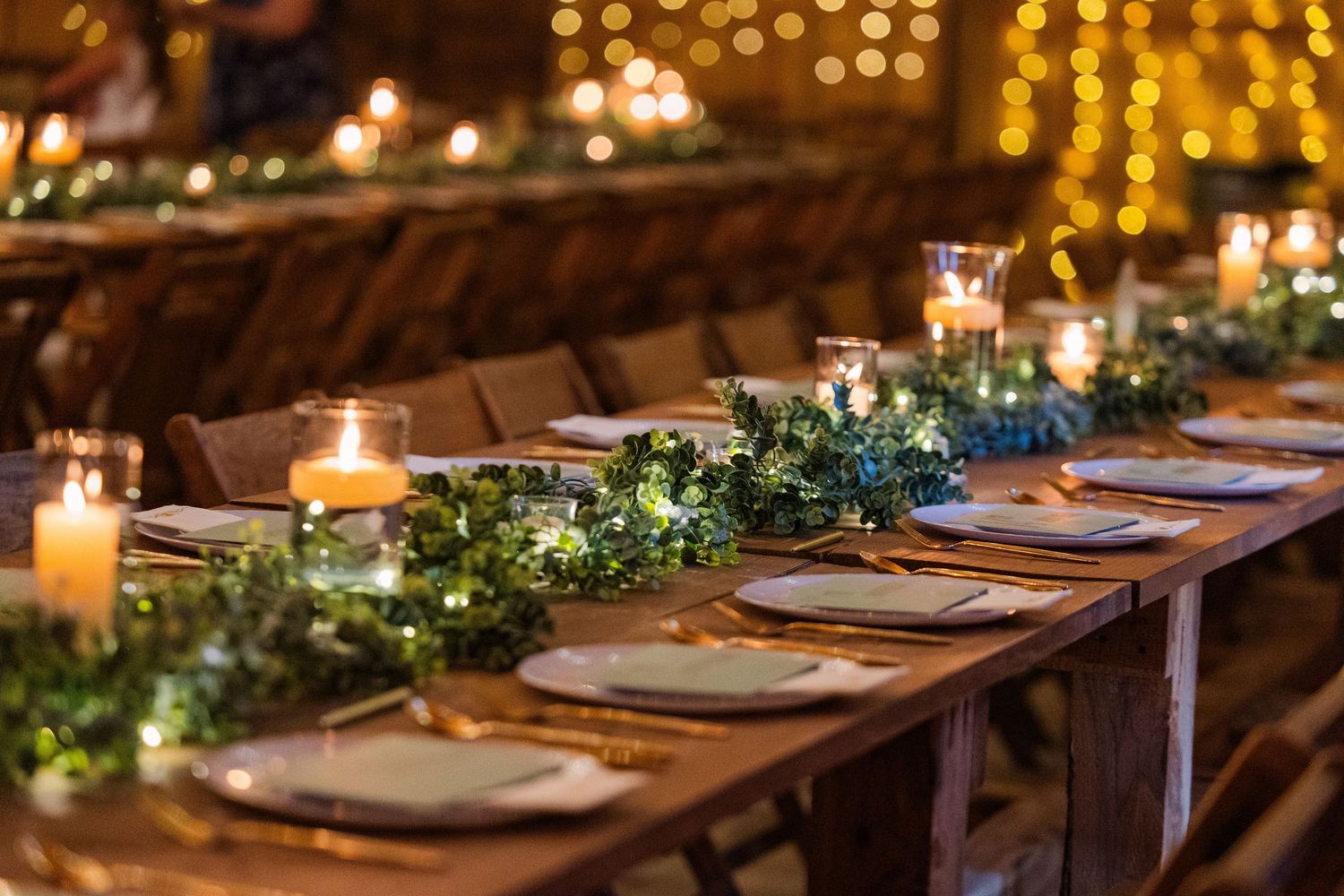 Rustic wedding reception table decorated with candlelight and greenery garlands.