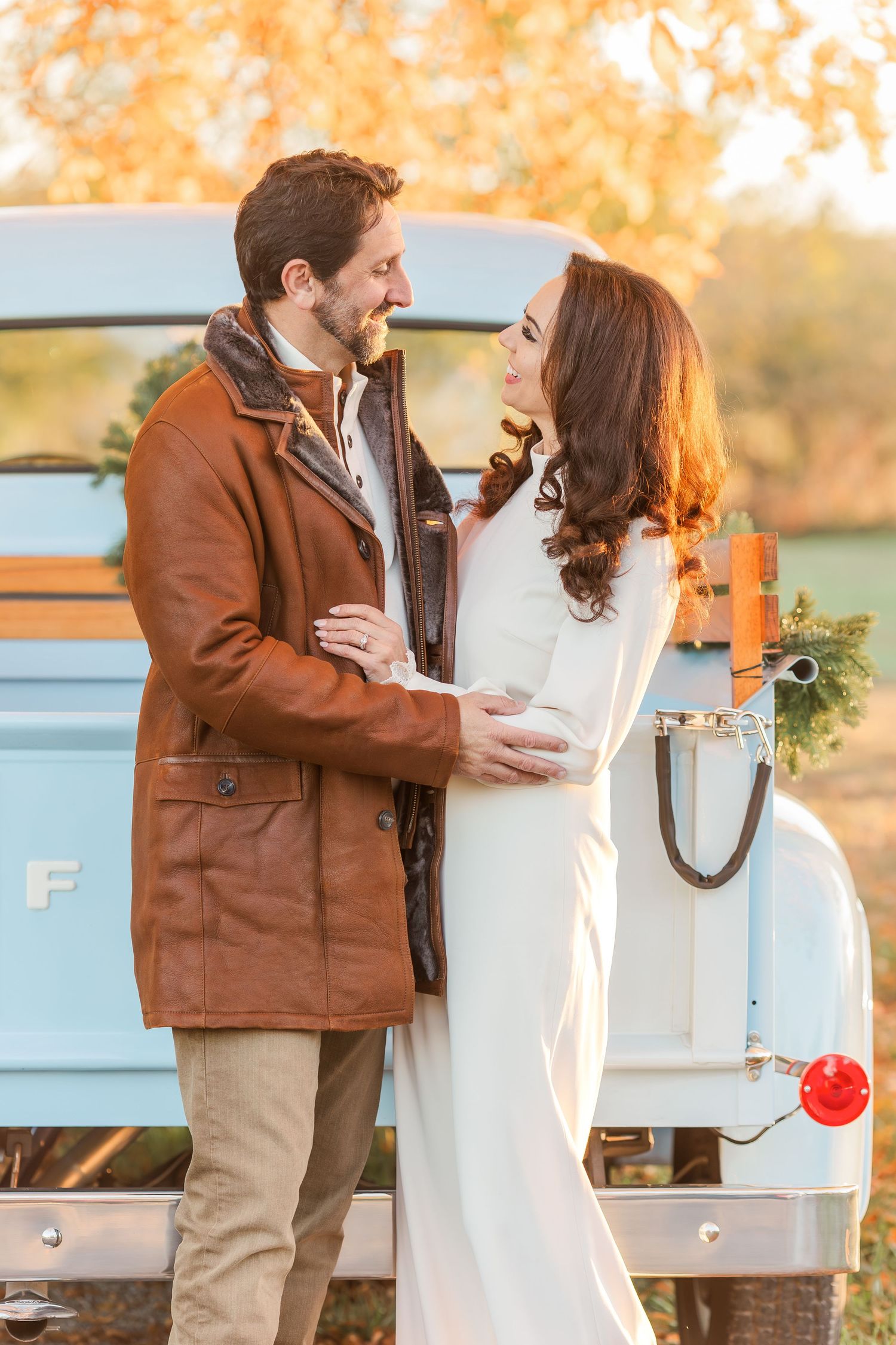 A couple shares a tender moment near a light blue vintage truck during golden hour.