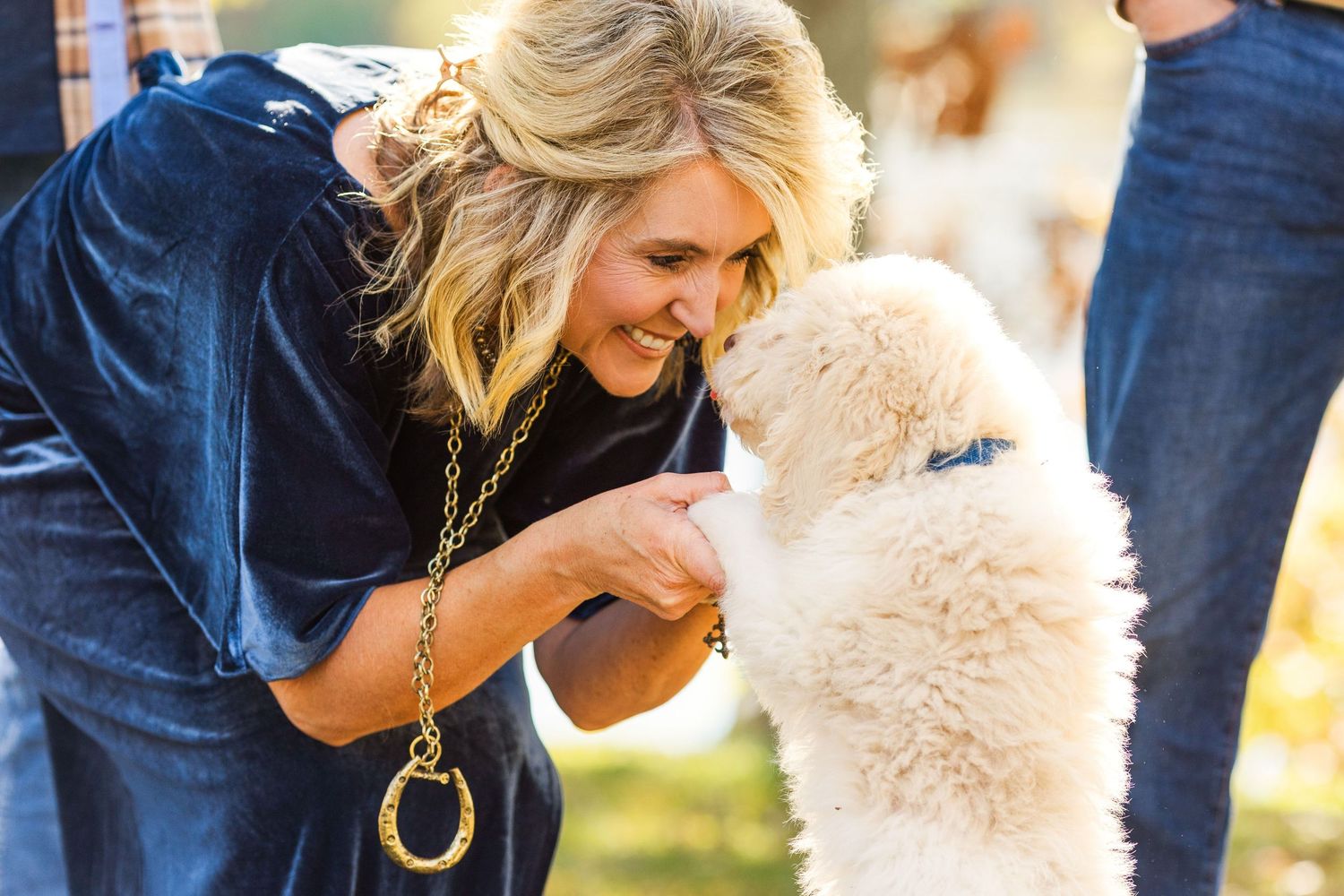 A candid moment of interaction between a person in navy and a small white puppy outdoors.