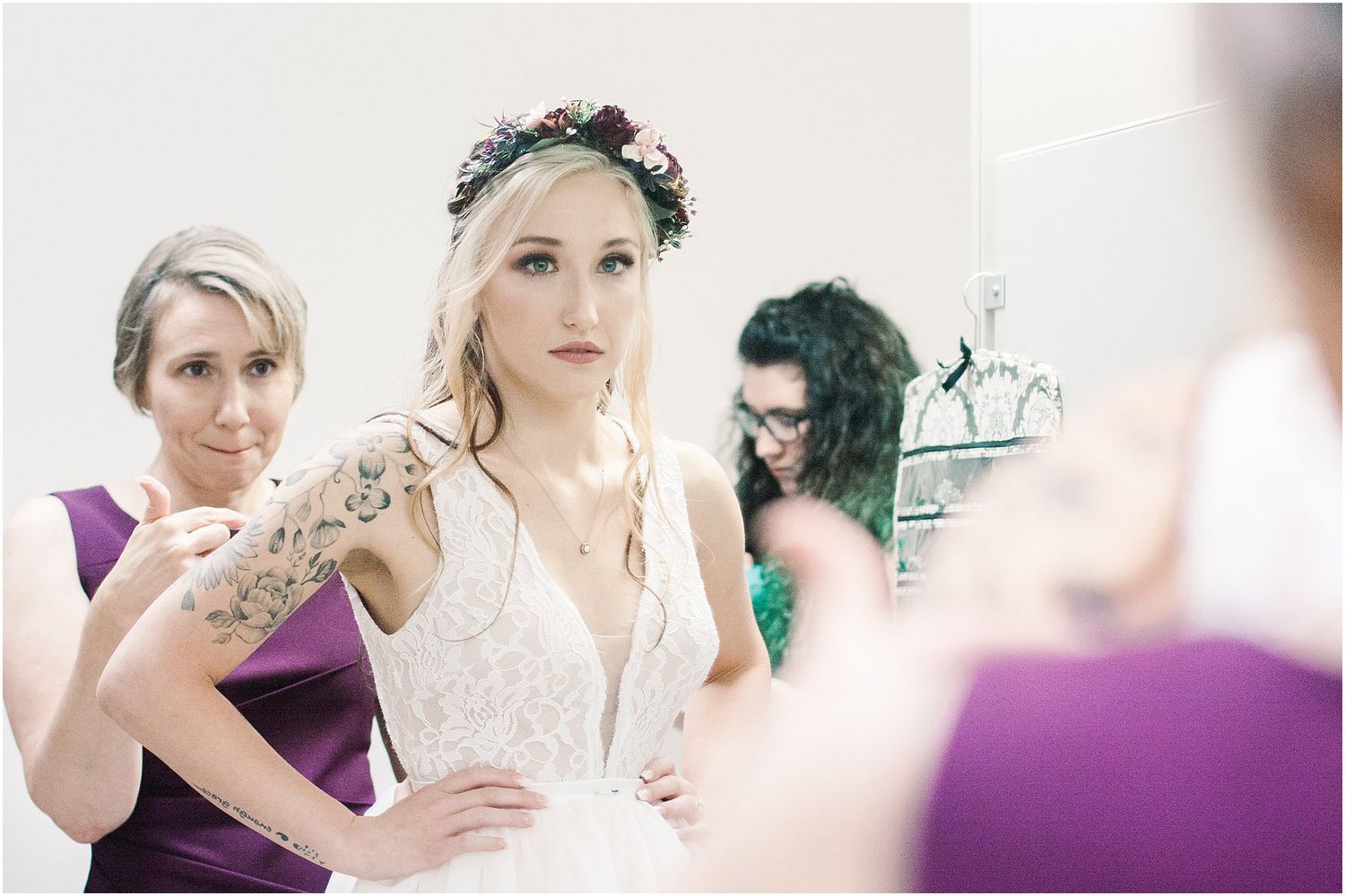 Wedding preparation scene with bridesmaids in purple dresses helping with final dress adjustments.