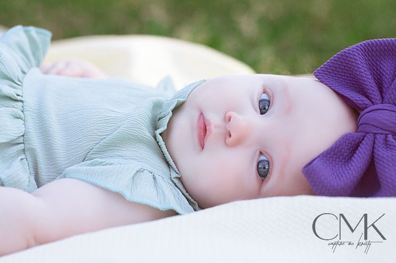 Close-up portrait of a baby wearing mint green outfit and purple bow lying down.