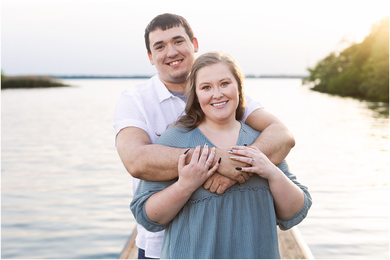Happy couple embracing at sunset by a waterfront with golden sunlight.