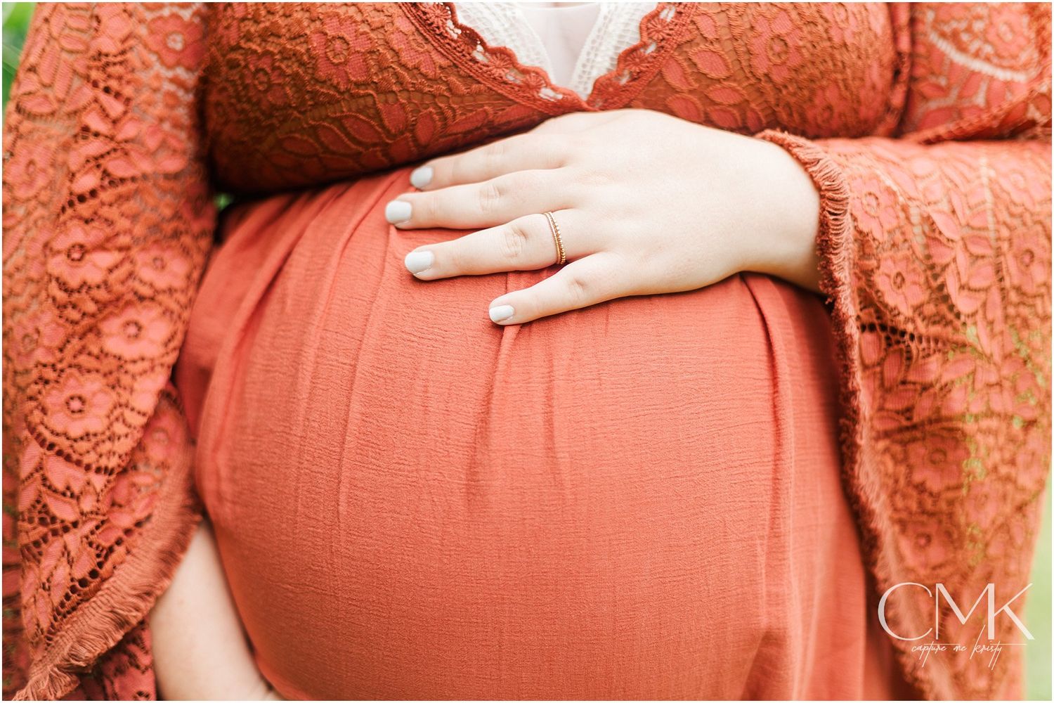 Hand resting on coral-colored maternity dress showing baby bump silhouette.