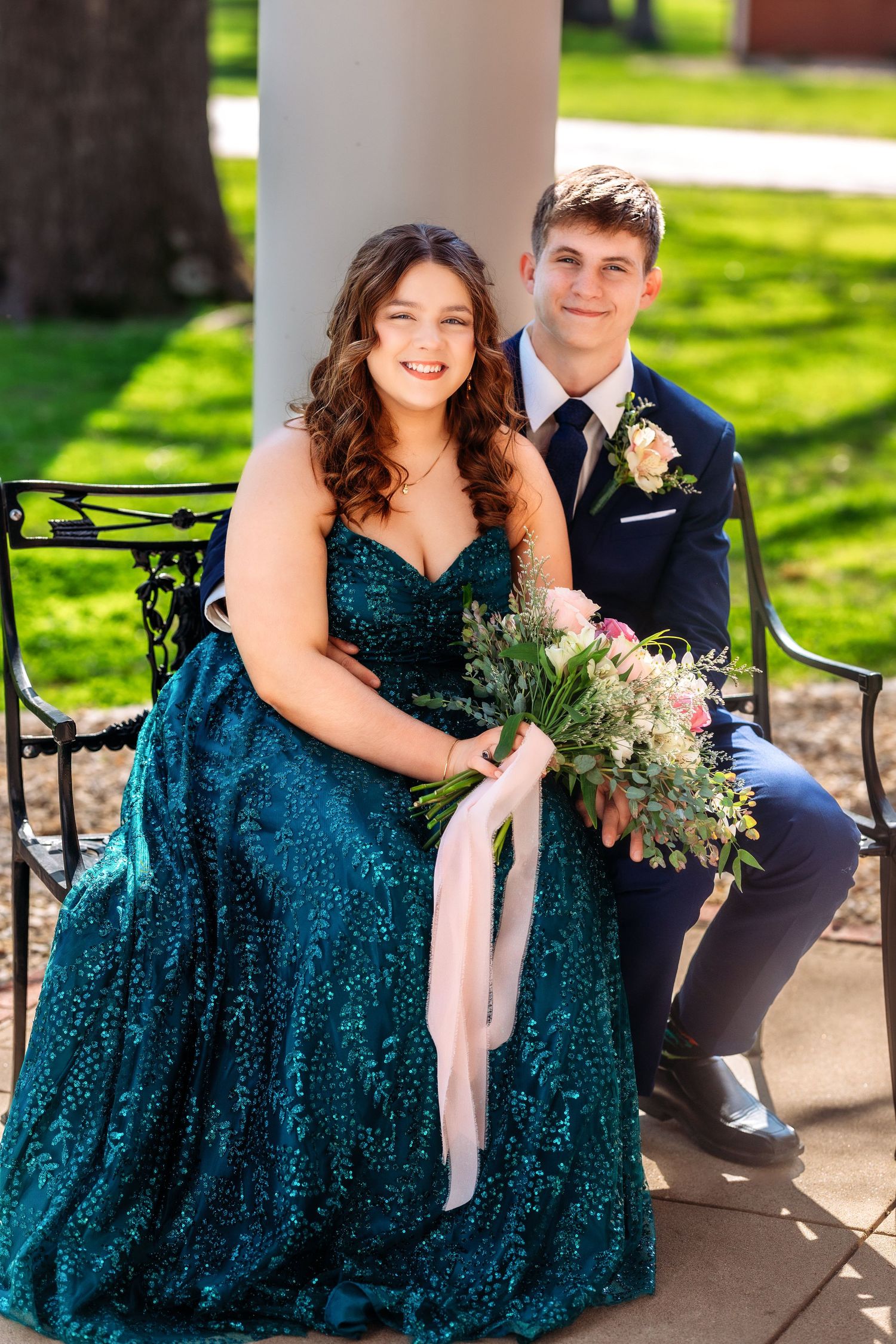 Couple in formal attire poses outdoors with bride wearing a sparkling emerald green sequin gown and holding floral bouquet.