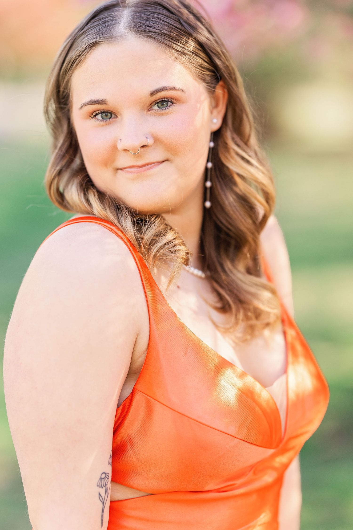 Woman in coral satin dress with wavy hair and dangling earrings poses outdoors.