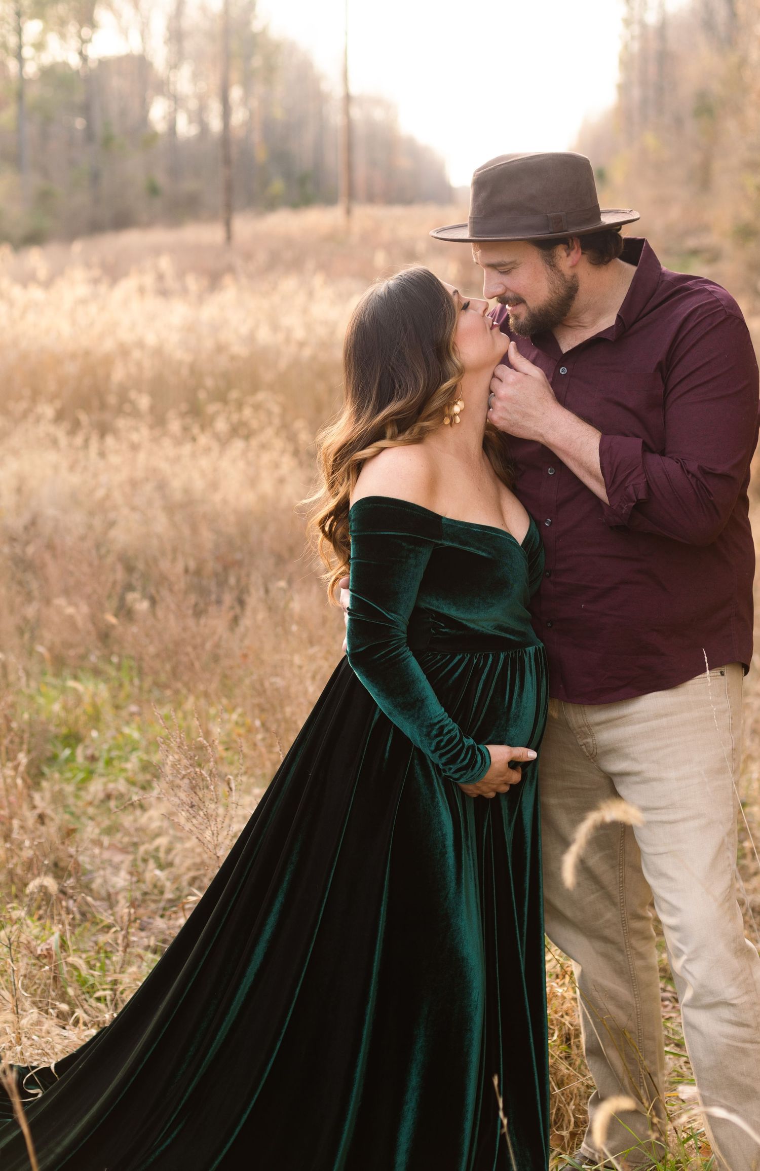 Intimate moment between couple during sunset maternity photoshoot in field.