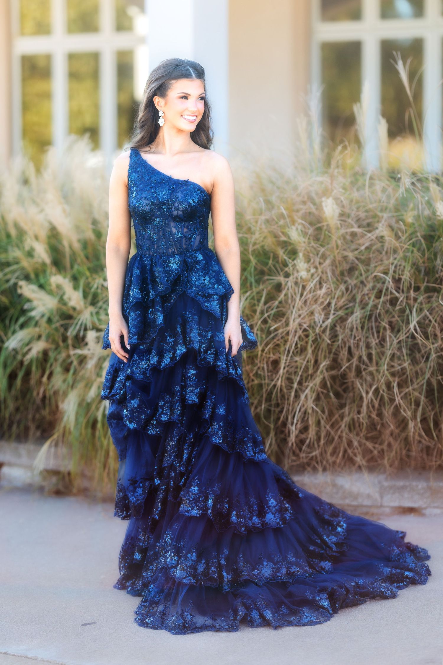 Full-length view of a one-shoulder navy blue lace gown with cascading ruffled tiers.