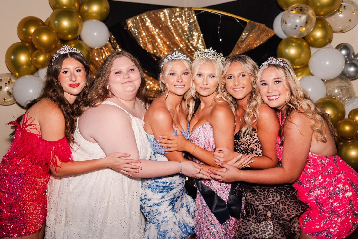 Group celebration photo with formal dresses and gold balloon decorations in the background.
