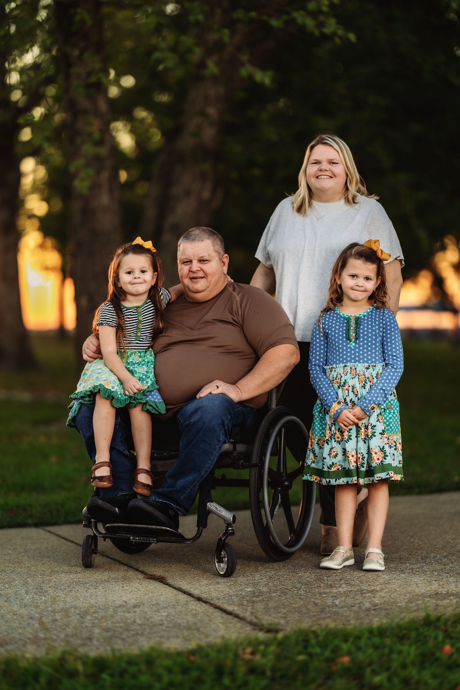 Family group poses together on pathway with wheelchair at sunset.