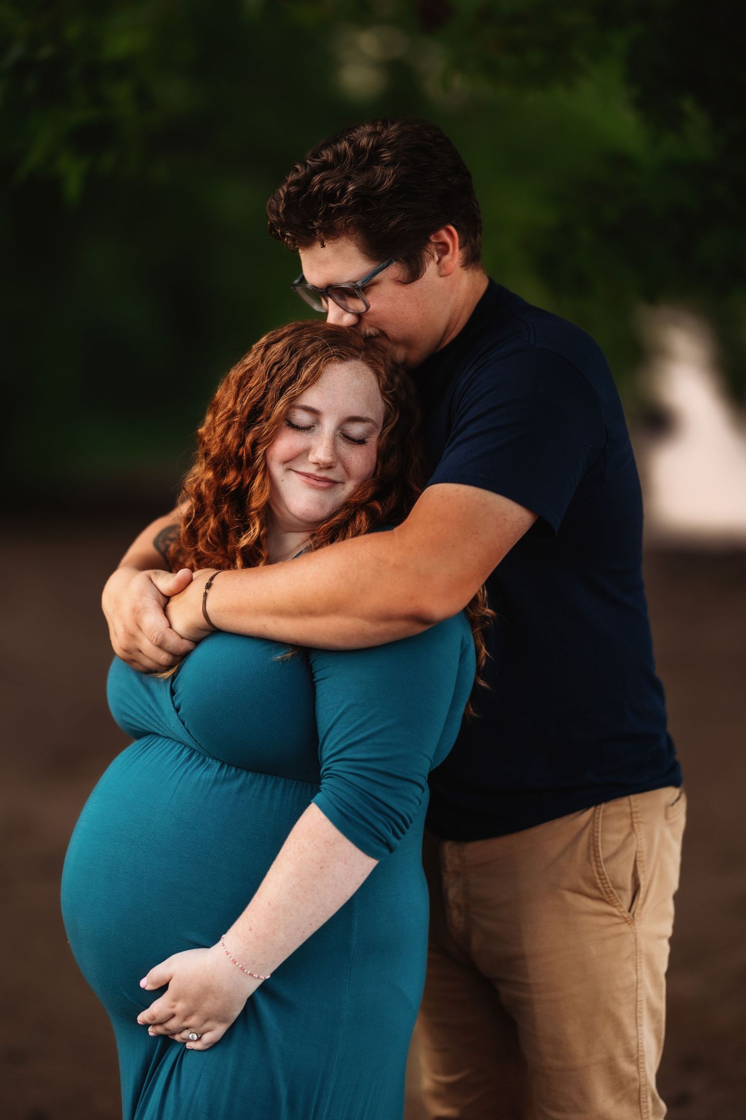 An intimate maternity portrait shows a couple embracing in teal and navy outfits.