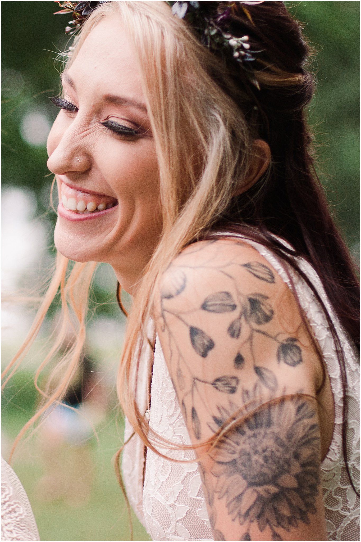 Close up of bride with floral crown and decorative arm tattoo smiling.