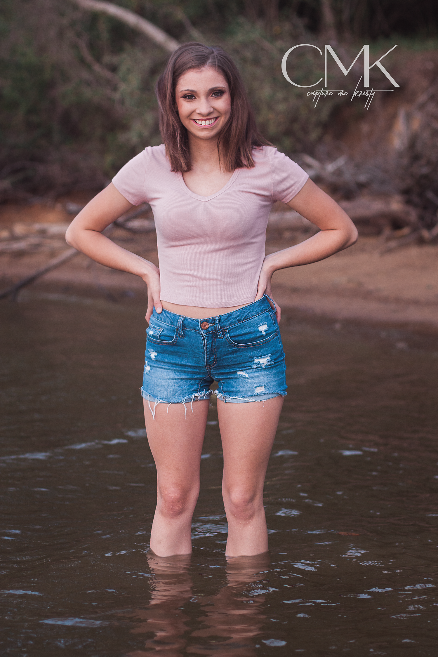 Summer portrait standing in shallow water wearing denim shorts and pink top.