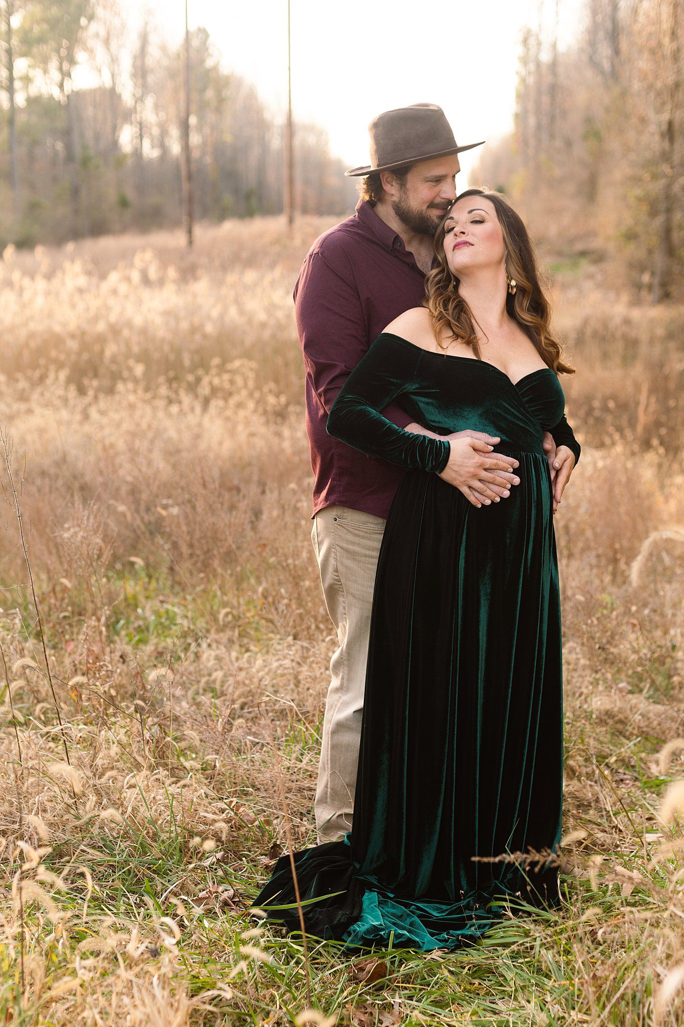 Intimate maternity moment captured outdoors with couple in velvet dress and burgundy shirt.