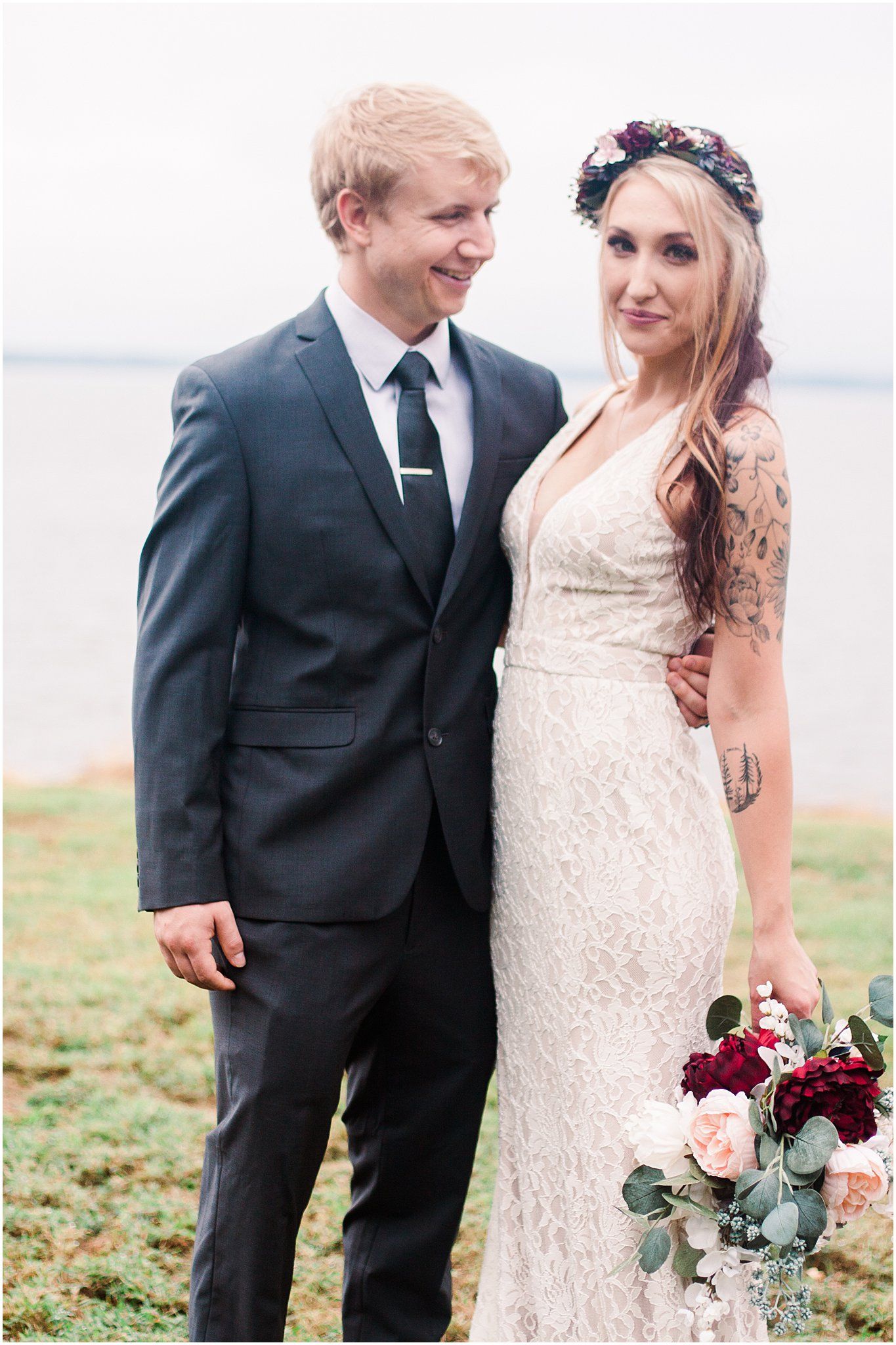 A wedding couple poses together outdoors with water in the background.