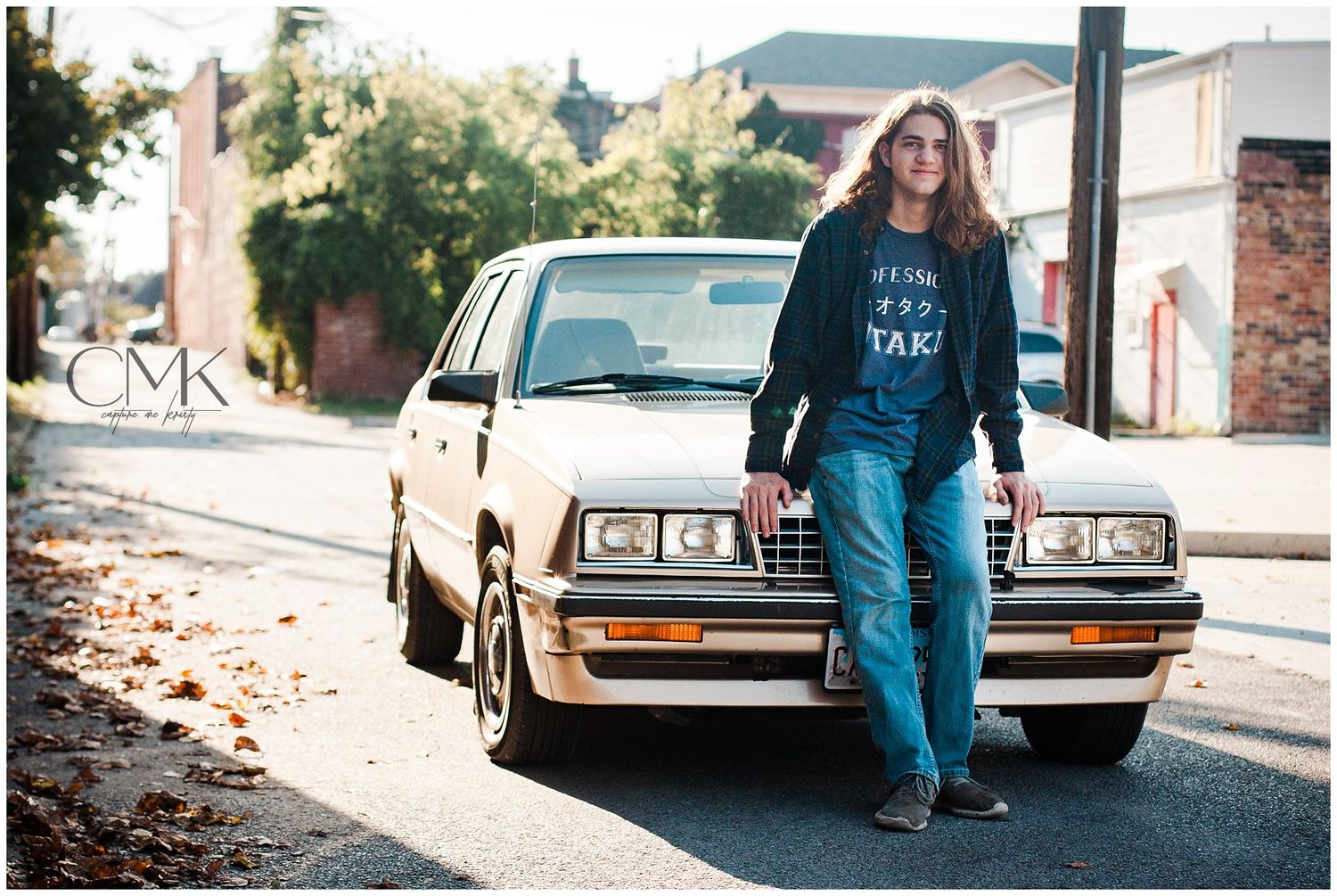 A casual street photo of someone standing in front of a classic car wearing jeans and a sweatshirt.