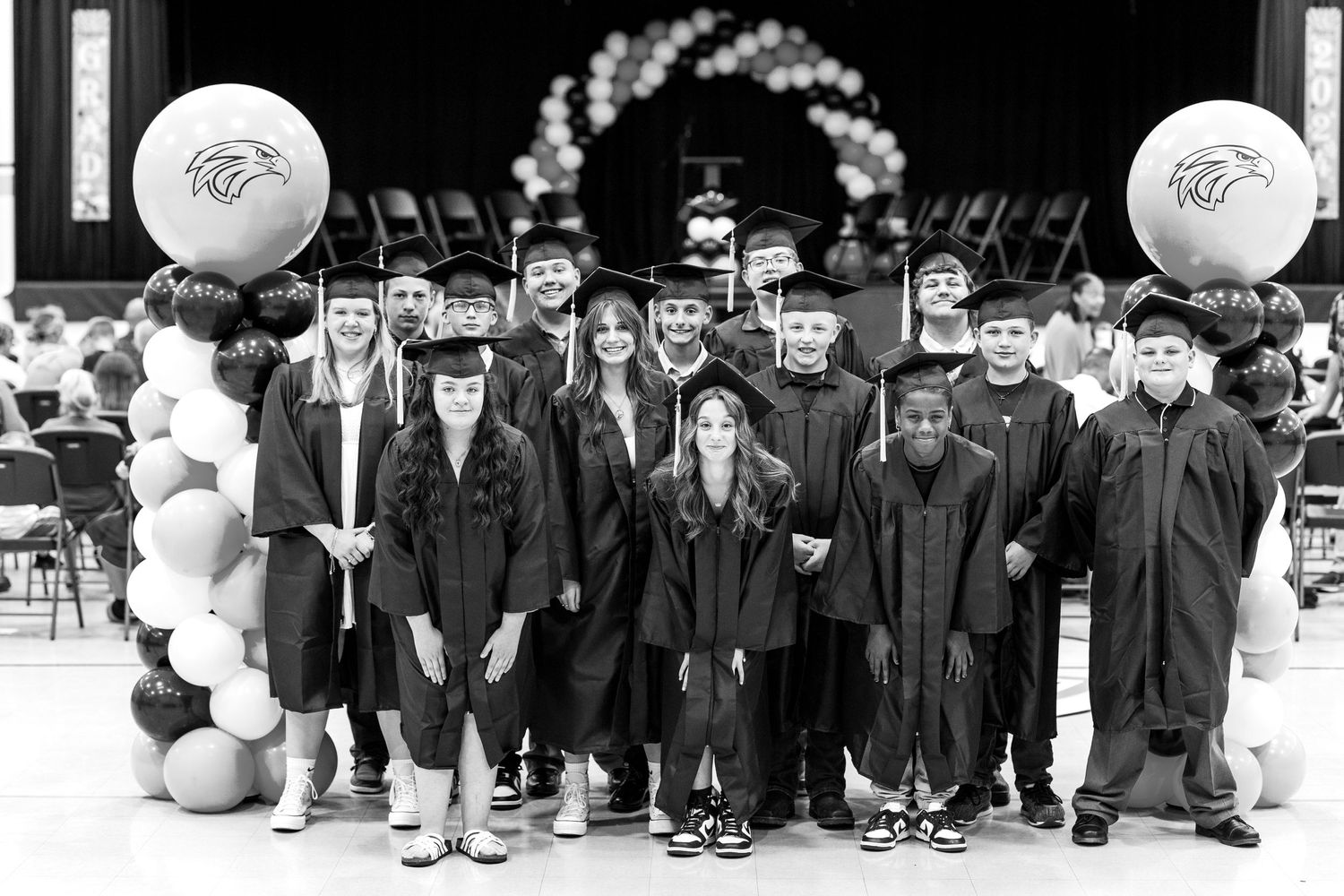 Black and white graduation photo showing graduates in caps and gowns with balloon decorations.