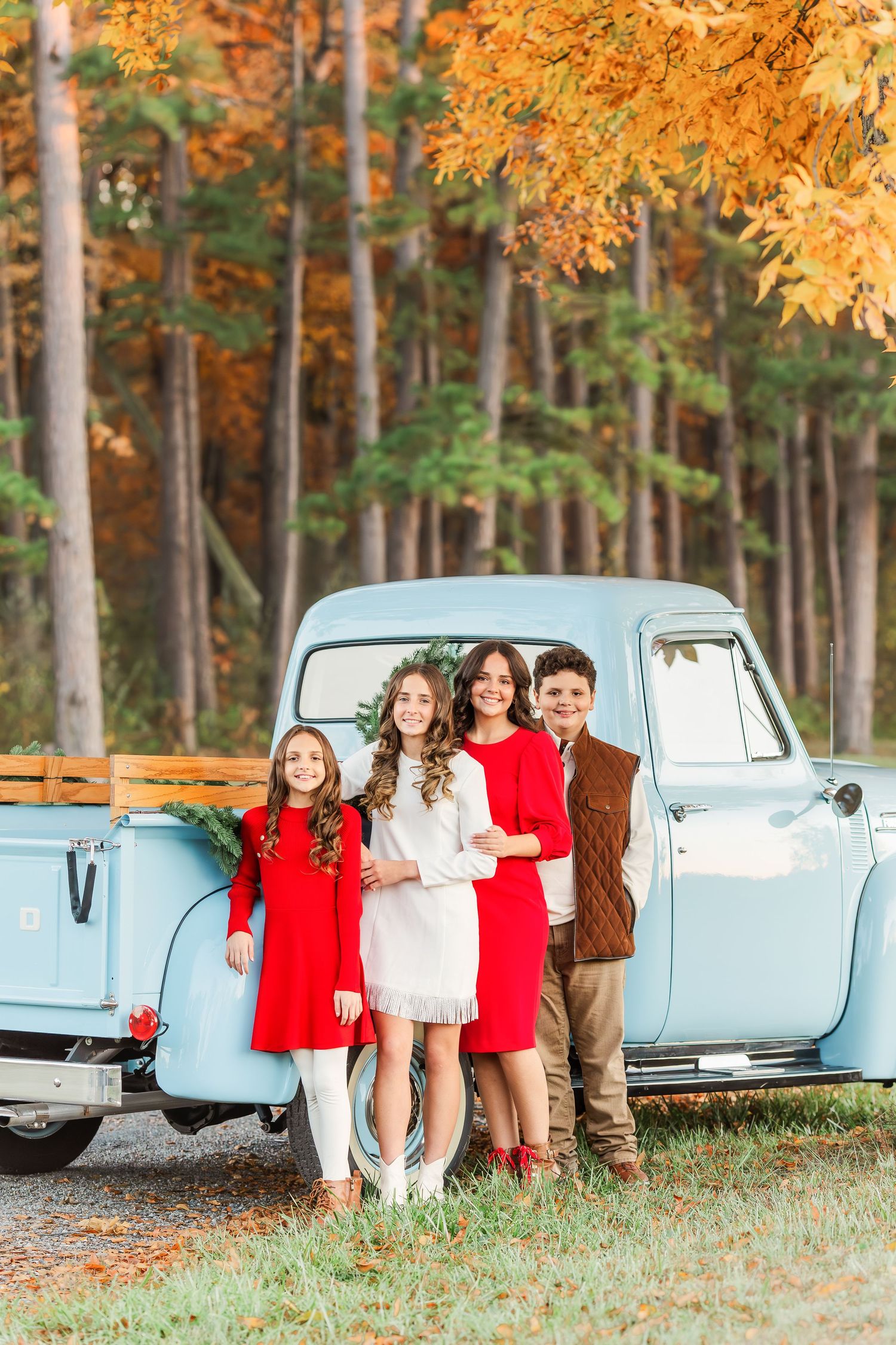 A light blue vintage truck serves as backdrop for a fall photo session with orange leaves overhead.