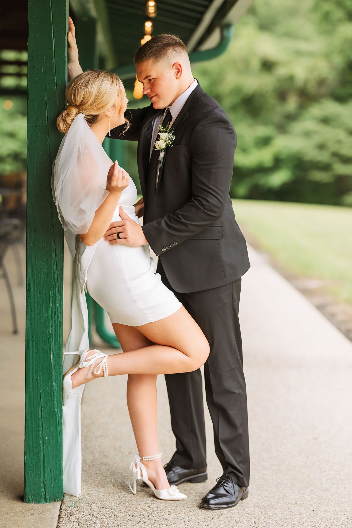 Couple in wedding attire sharing a playful moment under a covered walkway.