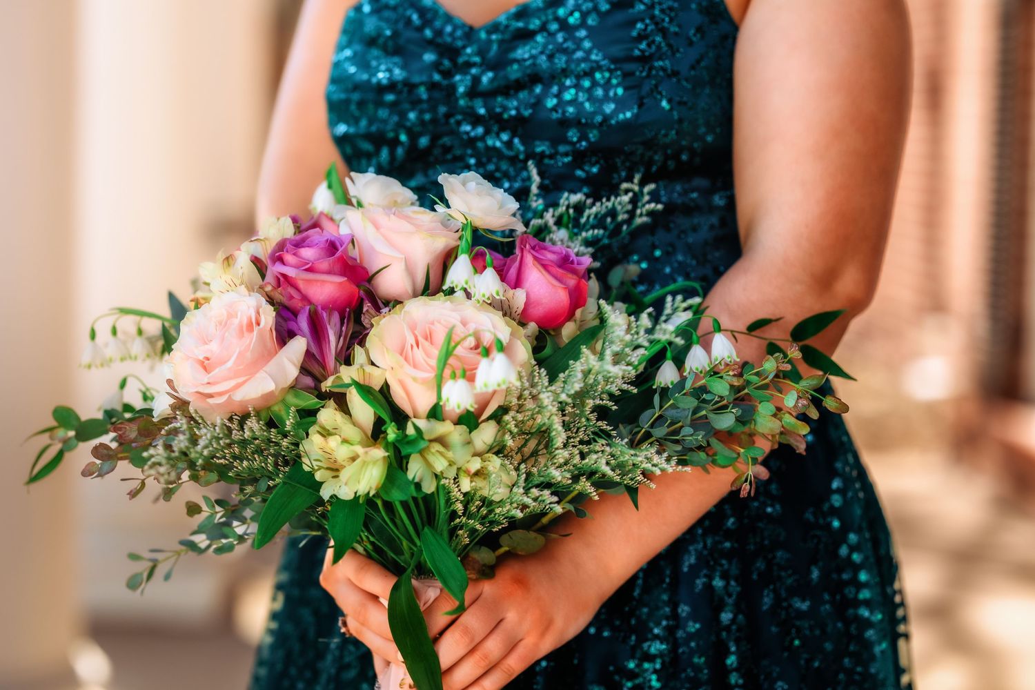 Hands holding a vibrant pink and white wedding bouquet against a teal sequined dress background.