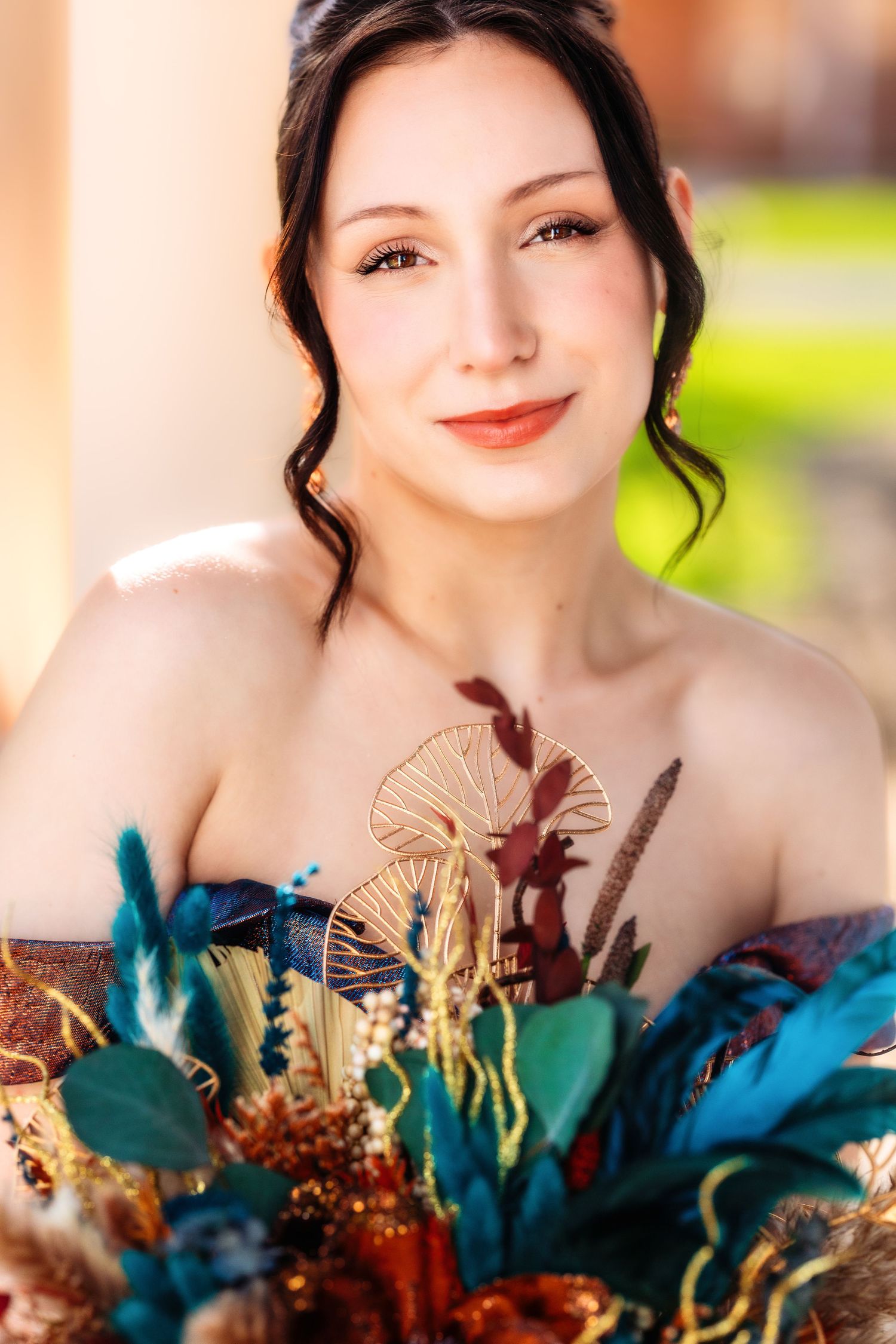 Close-up portrait with vibrant blue and teal dried floral bouquet featuring feathers and metallic accents.