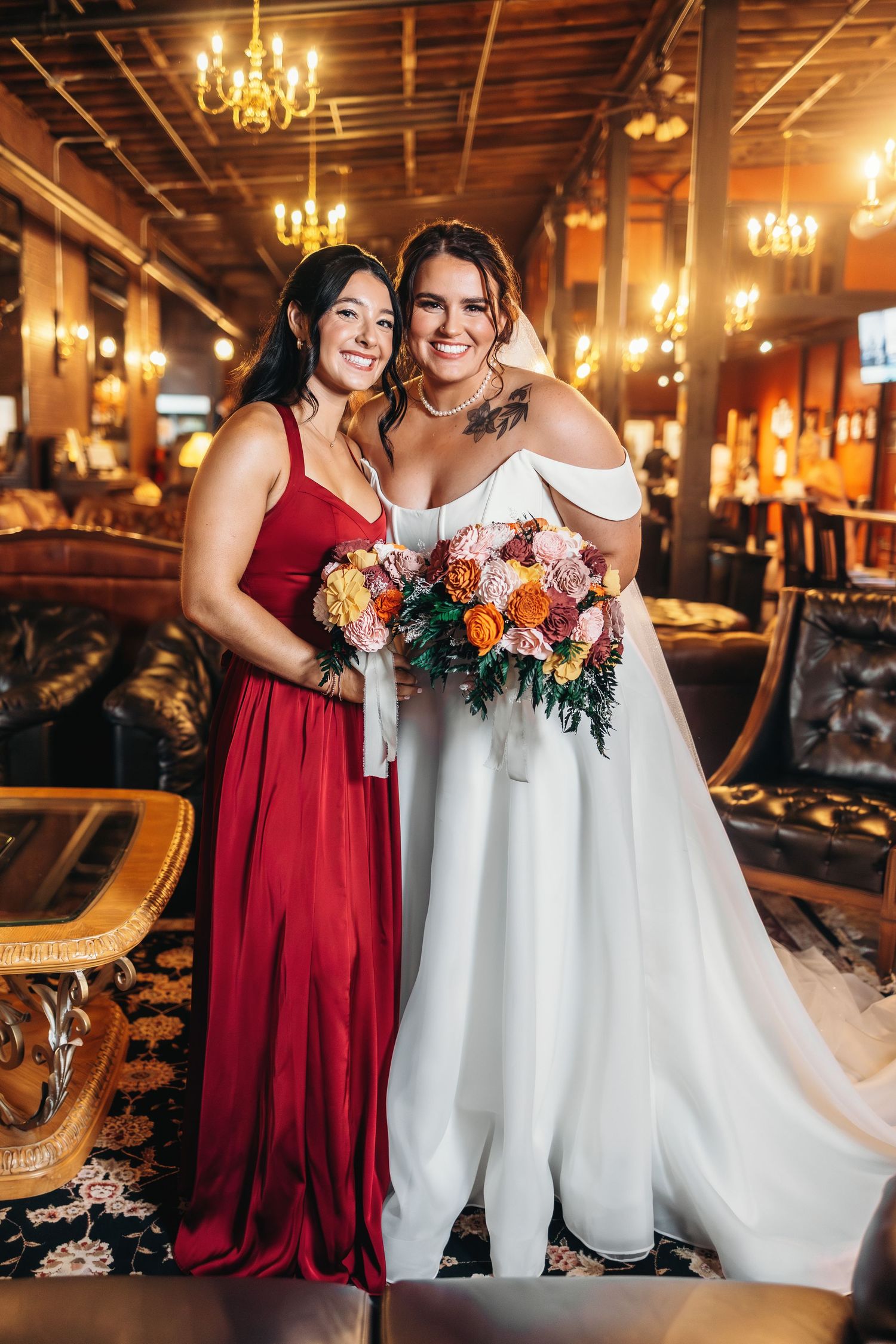 Wedding party members in burgundy dresses and white gowns pose together in an elegant venue with chandeliers.