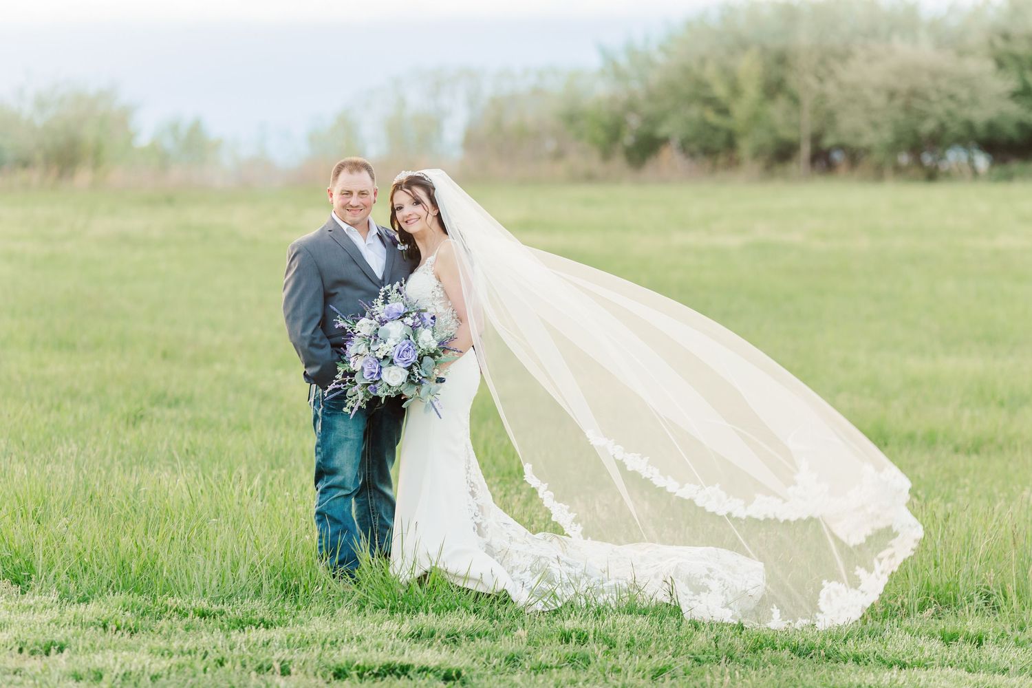 A flowing white wedding veil trails behind in a sunny green field.