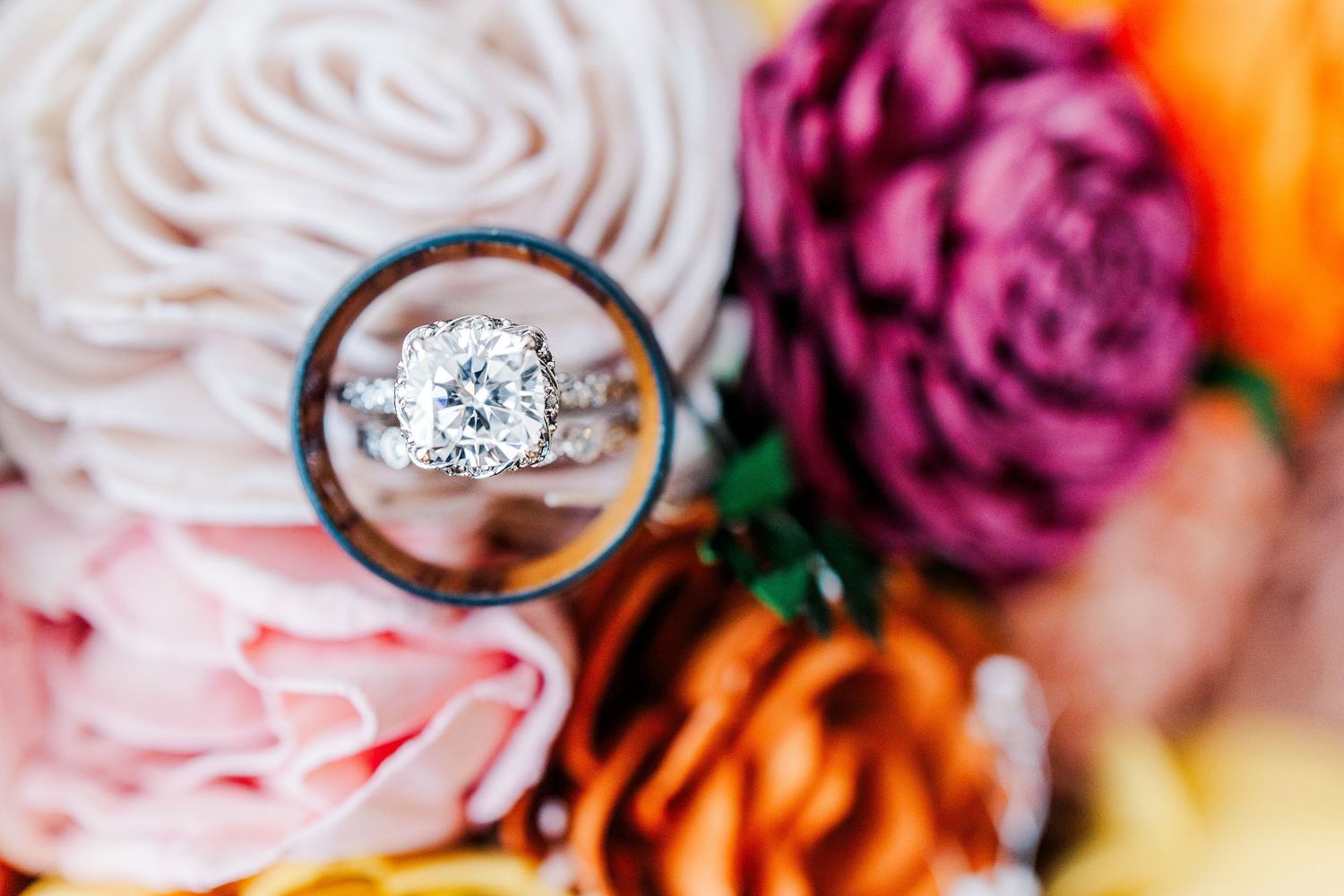 Wedding rings nestled among vibrant pink and orange flowers with soft focus background.