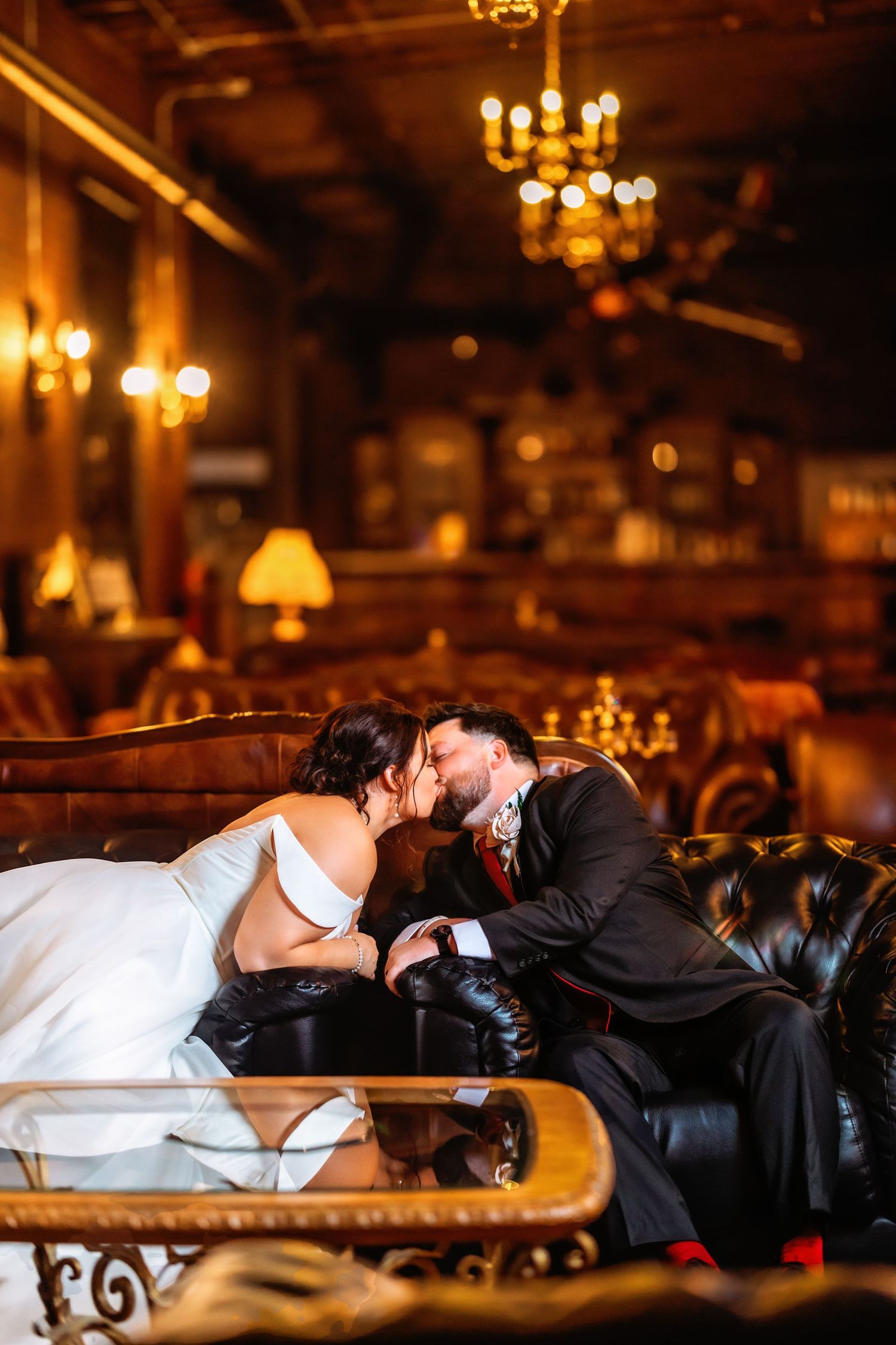 Romantic couple shares intimate moments on leather furniture under chandelier lighting.