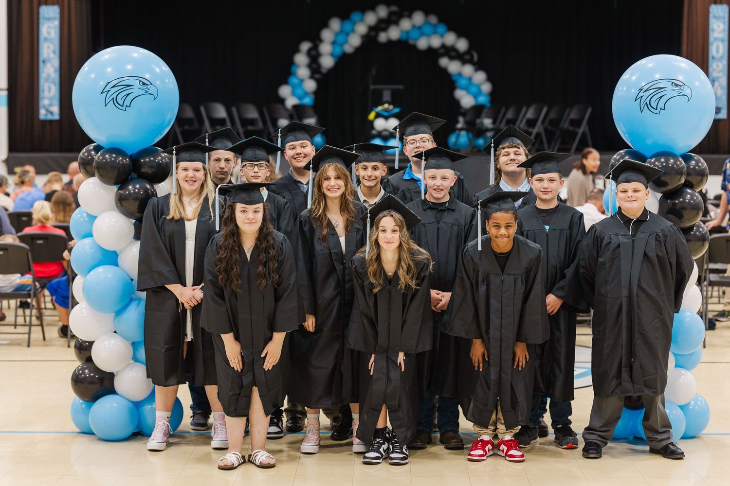 Graduates in black caps and gowns lined up for ceremony with blue balloon decorations.