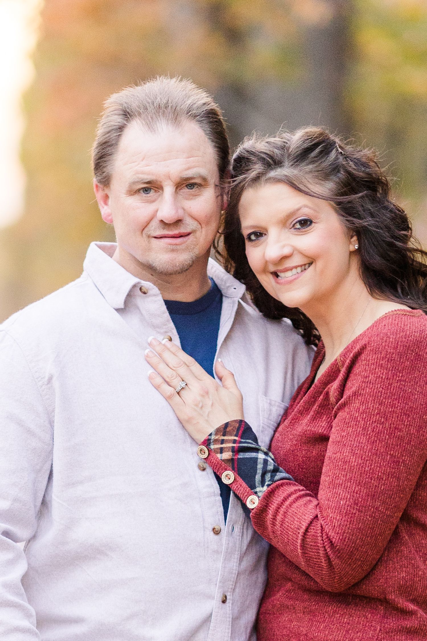 A couple in autumn outdoor setting with white and red sweaters smiling together during engagement photoshoot.