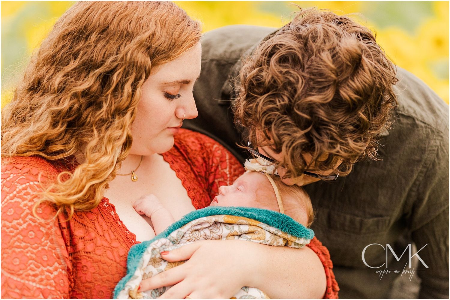 Intimate family moment captured while looking at baby wrapped in teal and patterned blanket.