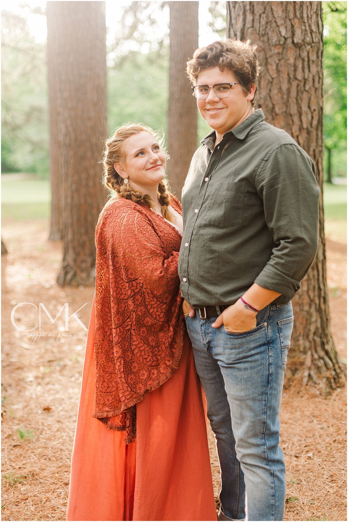 Couple standing together in a wooded setting for maternity photos.
