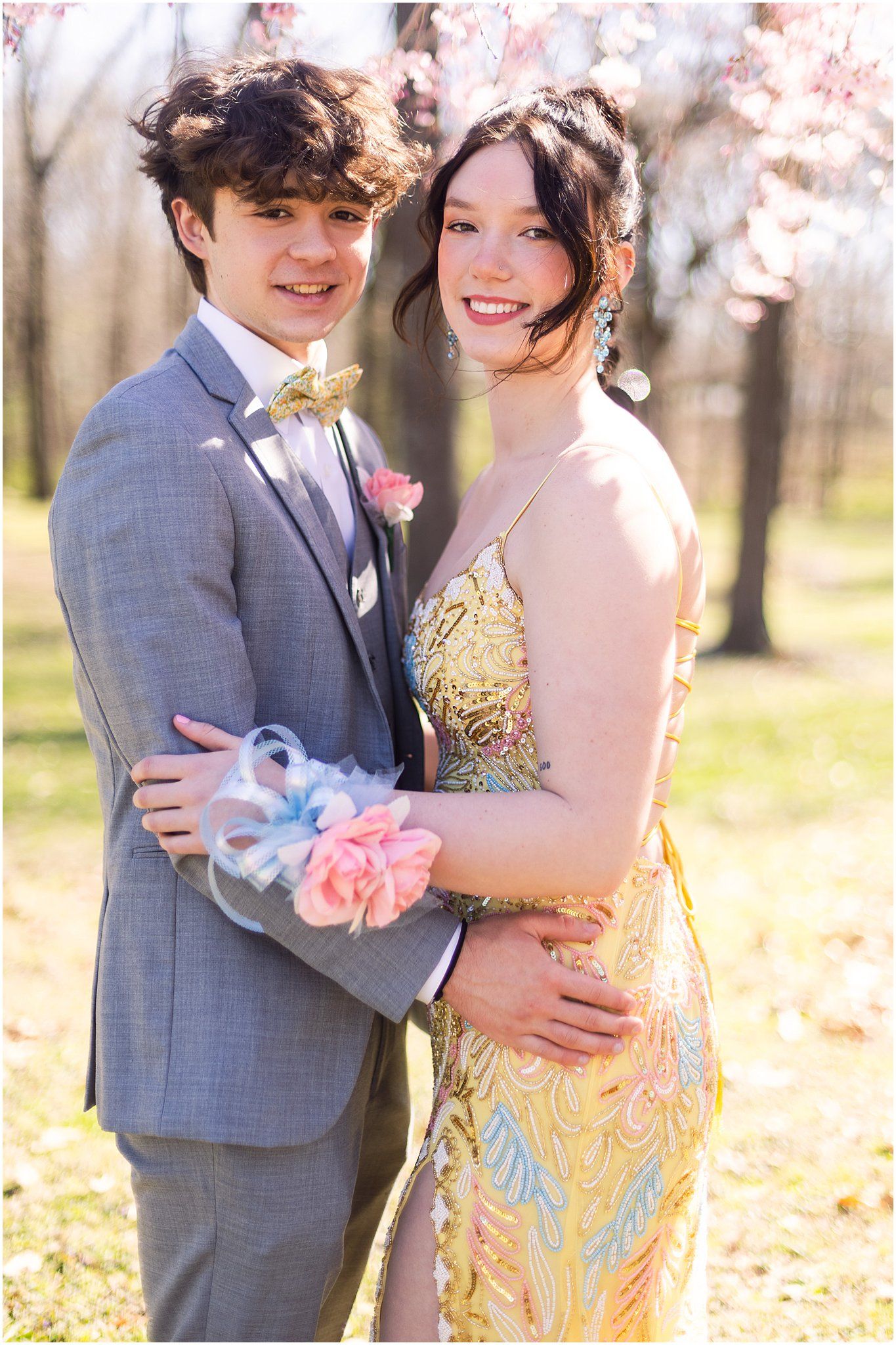 Happy couple in formal wear smiling together under spring cherry blossoms.