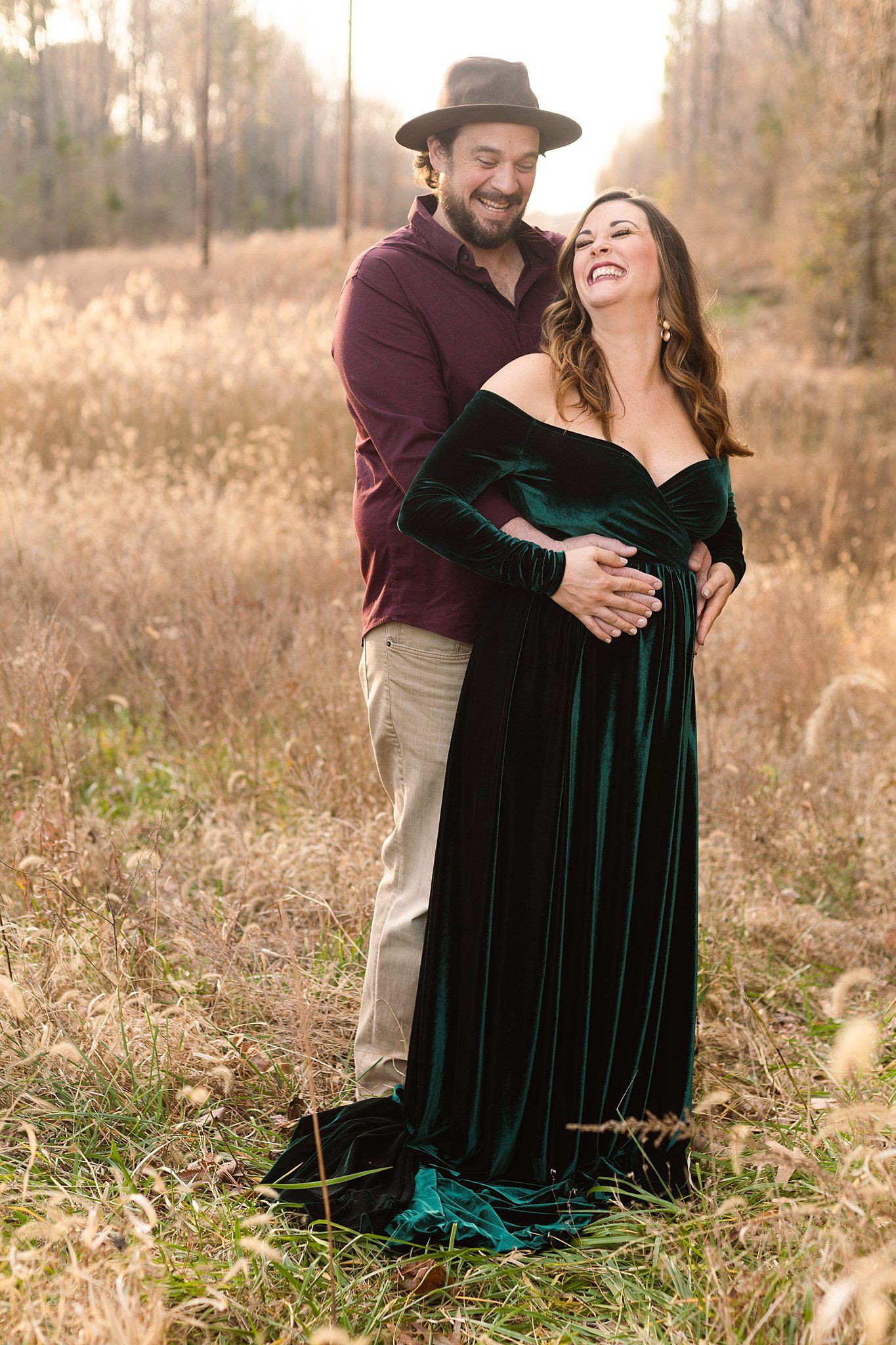 Happy couple sharing a laugh during maternity photoshoot in golden fall field.