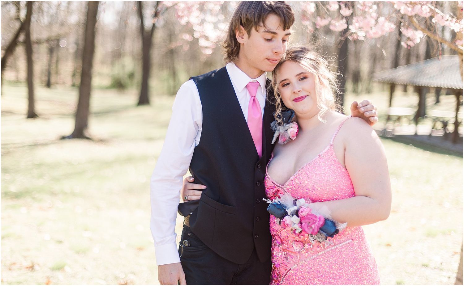 Candid moment captured of a couple in formal wear beneath blooming cherry trees.