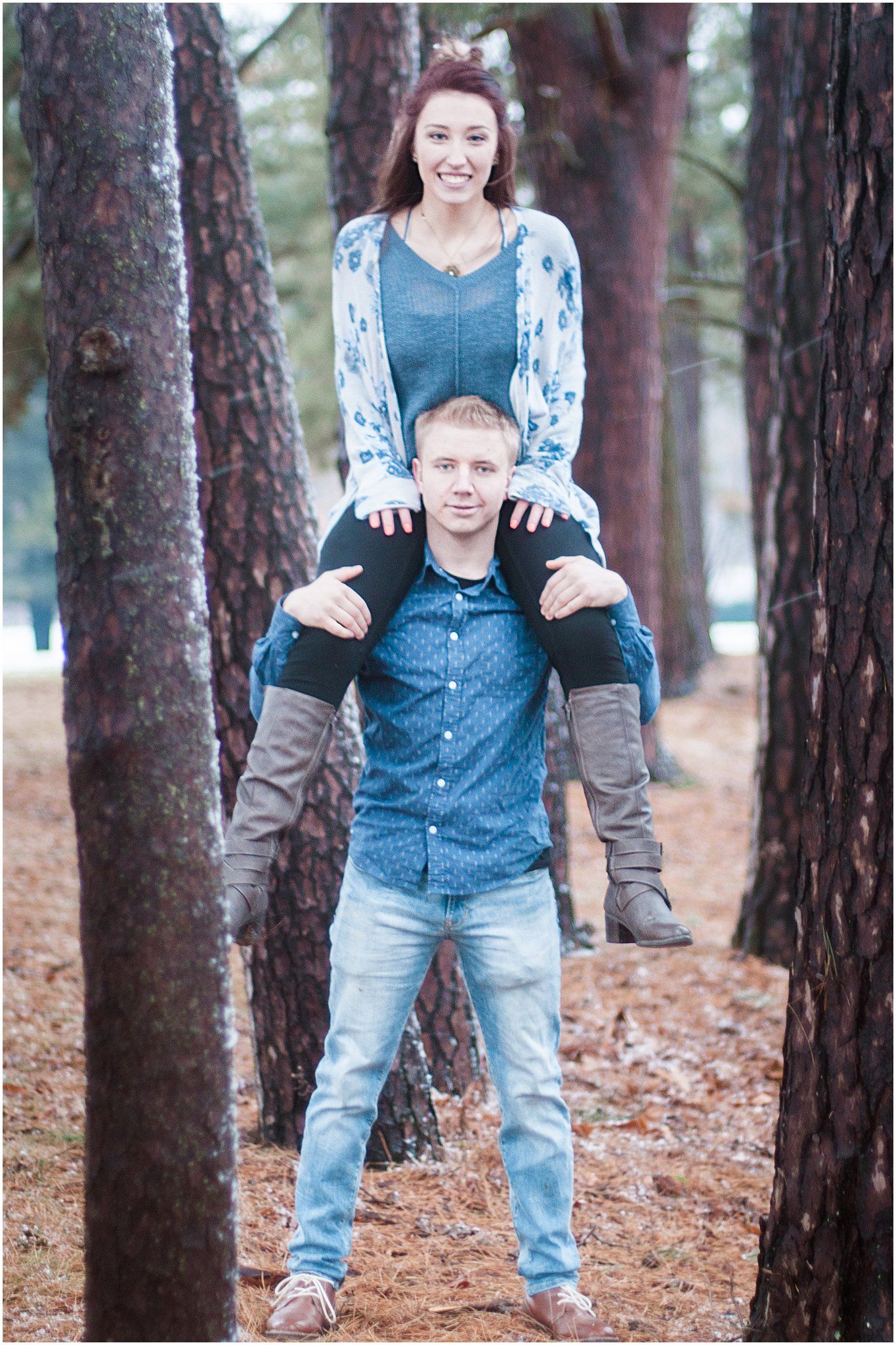 Playful couple having fun with piggyback ride in a pine forest during winter.
