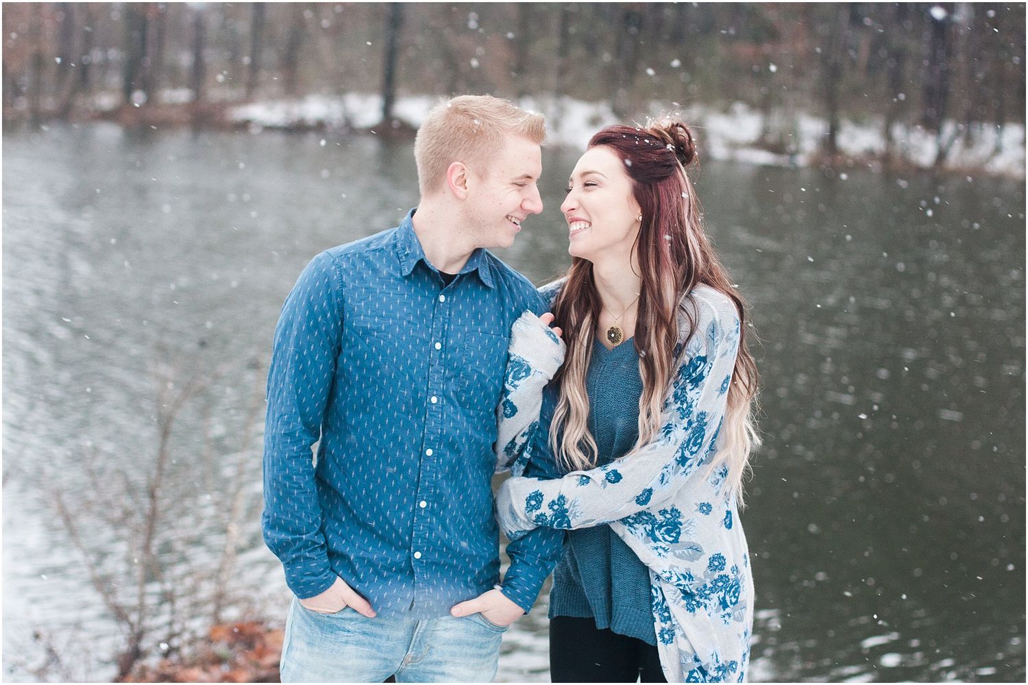 A couple sharing a lighthearted moment in winter attire by a lake.