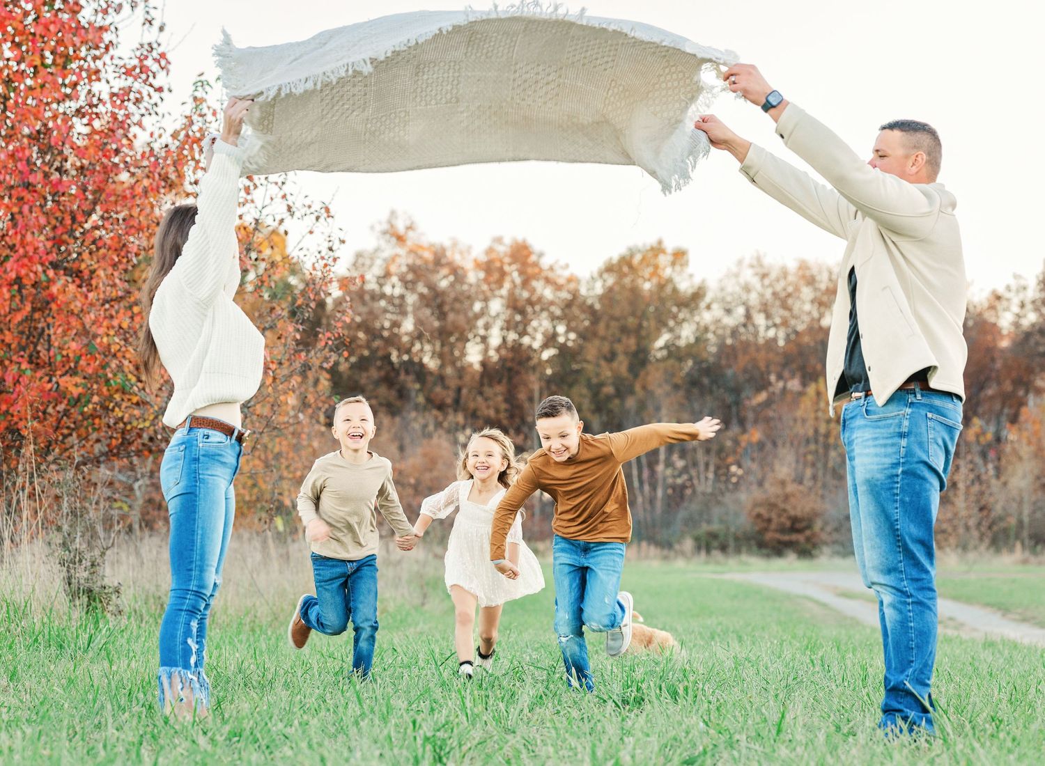 Family plays and runs together through tall grass at sunset.