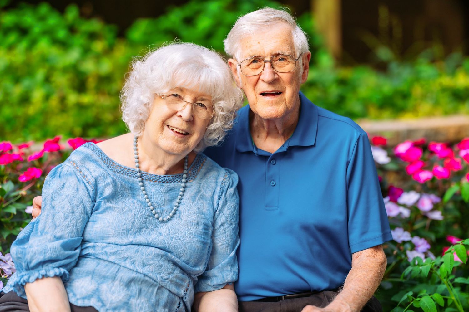 Senior couple sharing loving moments together in a garden with vibrant pink flowers.