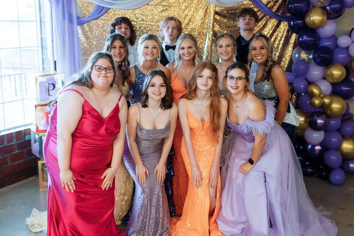 A group wearing formal attire in purple, orange, and red dresses pose together at an event.