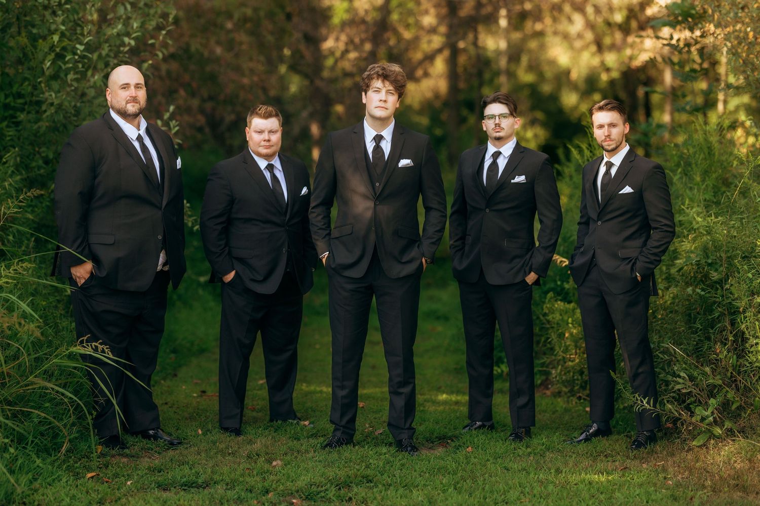 Groomsmen in matching black suits stand together for formal wedding photos.