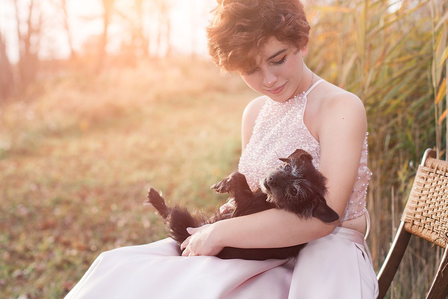Person in pink formal dress cuddles with black cat outdoors.