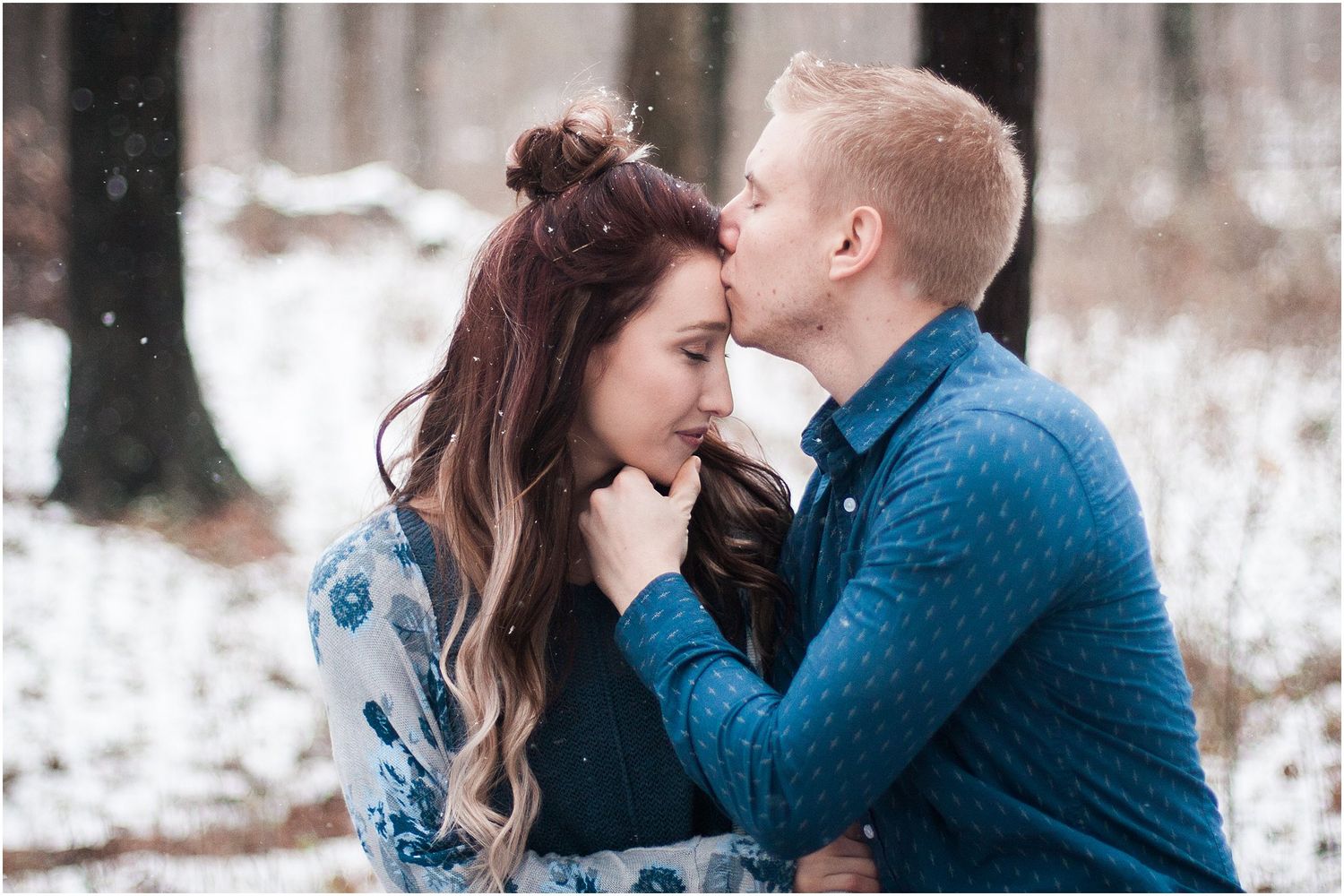 Intimate winter moment between couple in blue outfits with snow falling in background.